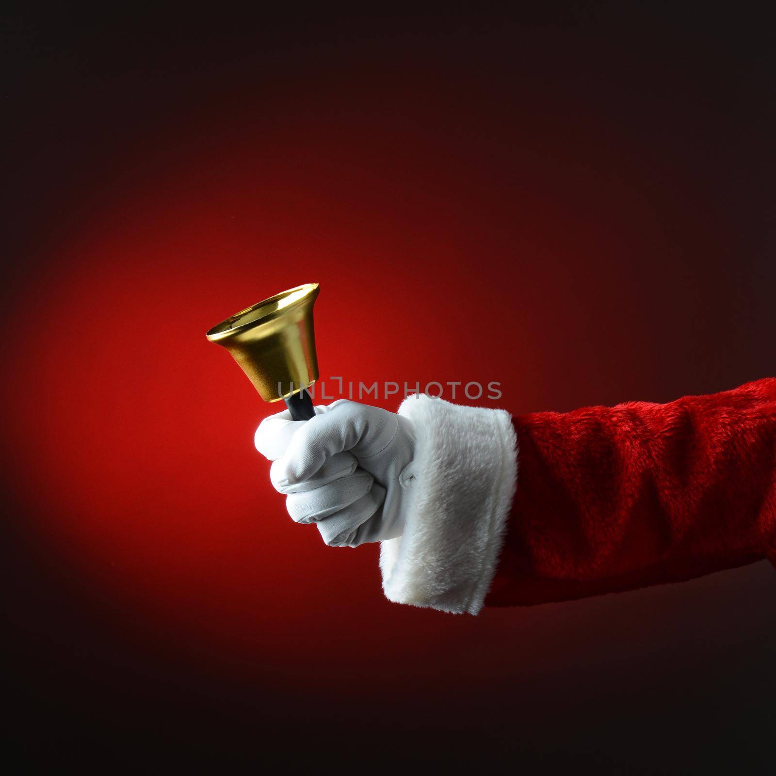 Santa Claus ringing a bell over dark red background. Square Format, only hand and arm are visible.