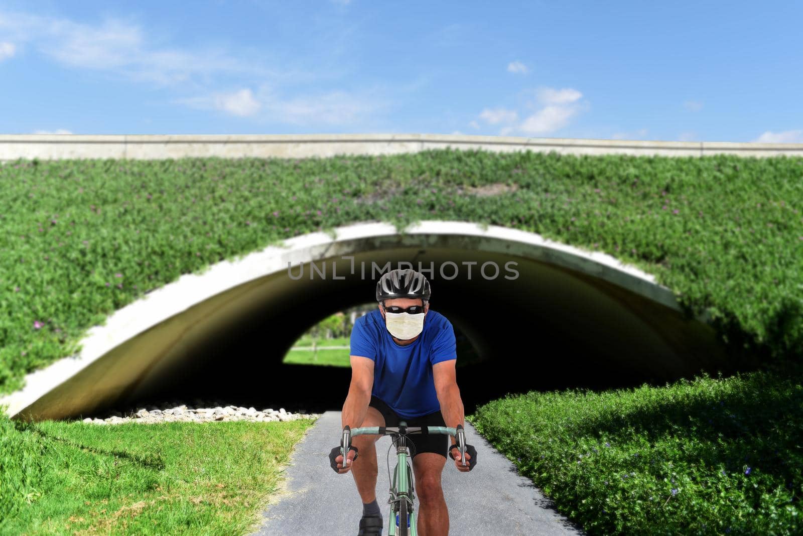 Cyclist on a bike path wearing a COVID-19 surgical mask. by sCukrov
