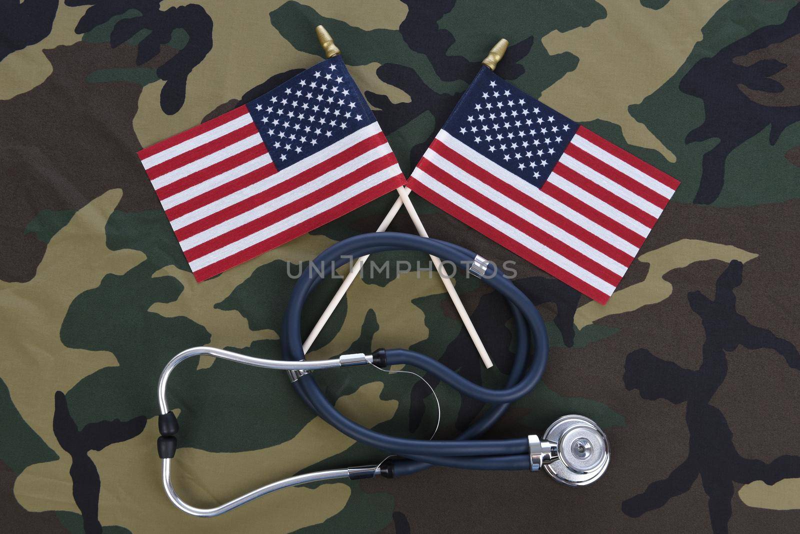 Military Health Care Concept. Camouflage background with stethoscope and two crossed American flags.