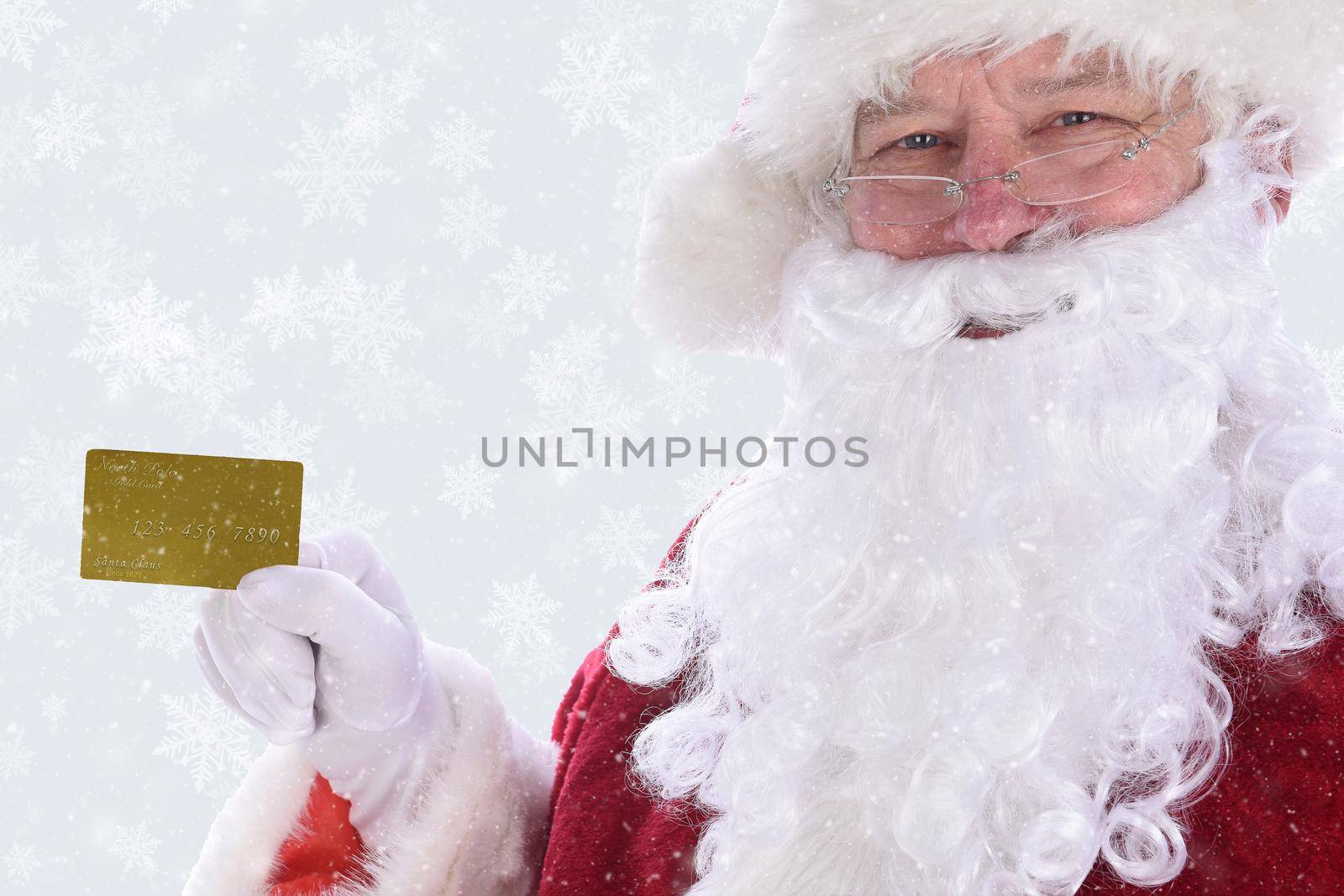 Closeup of Santa Claus holding his personal Noth Pole Gold Credit Card, with Winter Snow flakes on a silver background. 