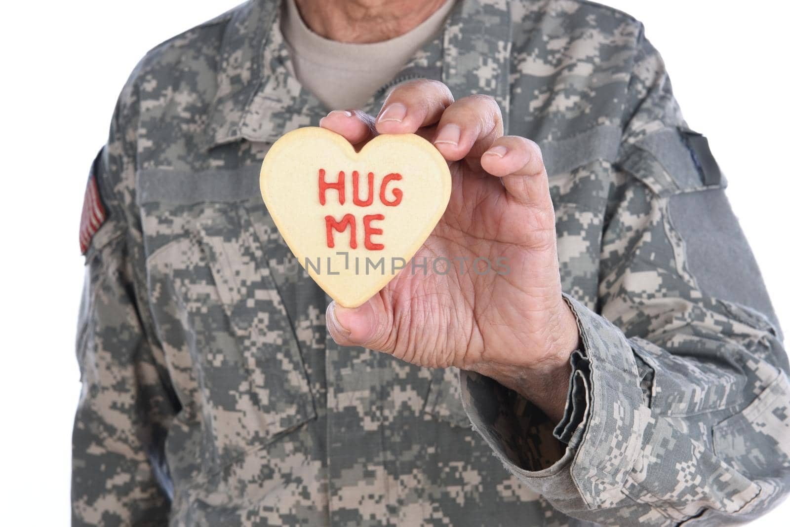 Closeup of a soldier holding a Heart Shaped Valentines Day cookie with the words Hug Me written in red icing.  by sCukrov
