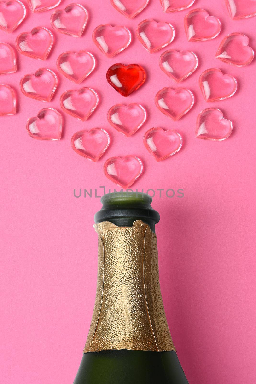 Valentines Day Concept: high angle shot of a white champagne bottle with pink glass hearts simulating a spray. by sCukrov