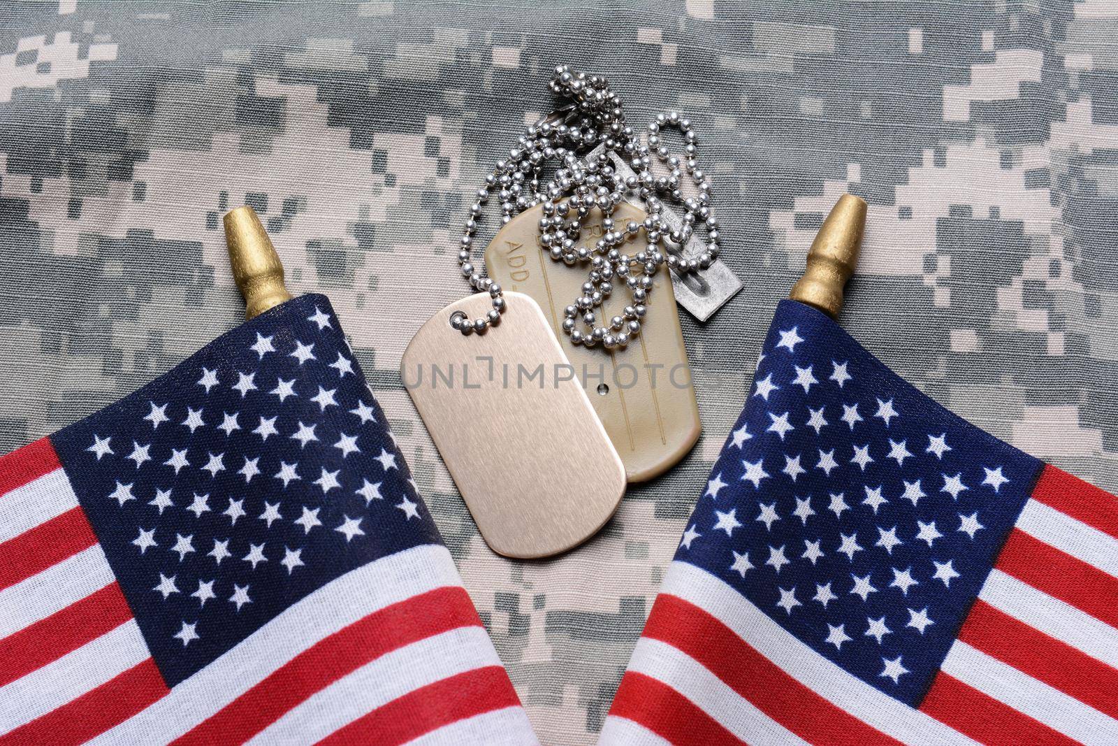 Closeup of two crossed American Flags on camouflage material with dog tags in the middle. The ID tags are blank. Horizontal format filling the frame.