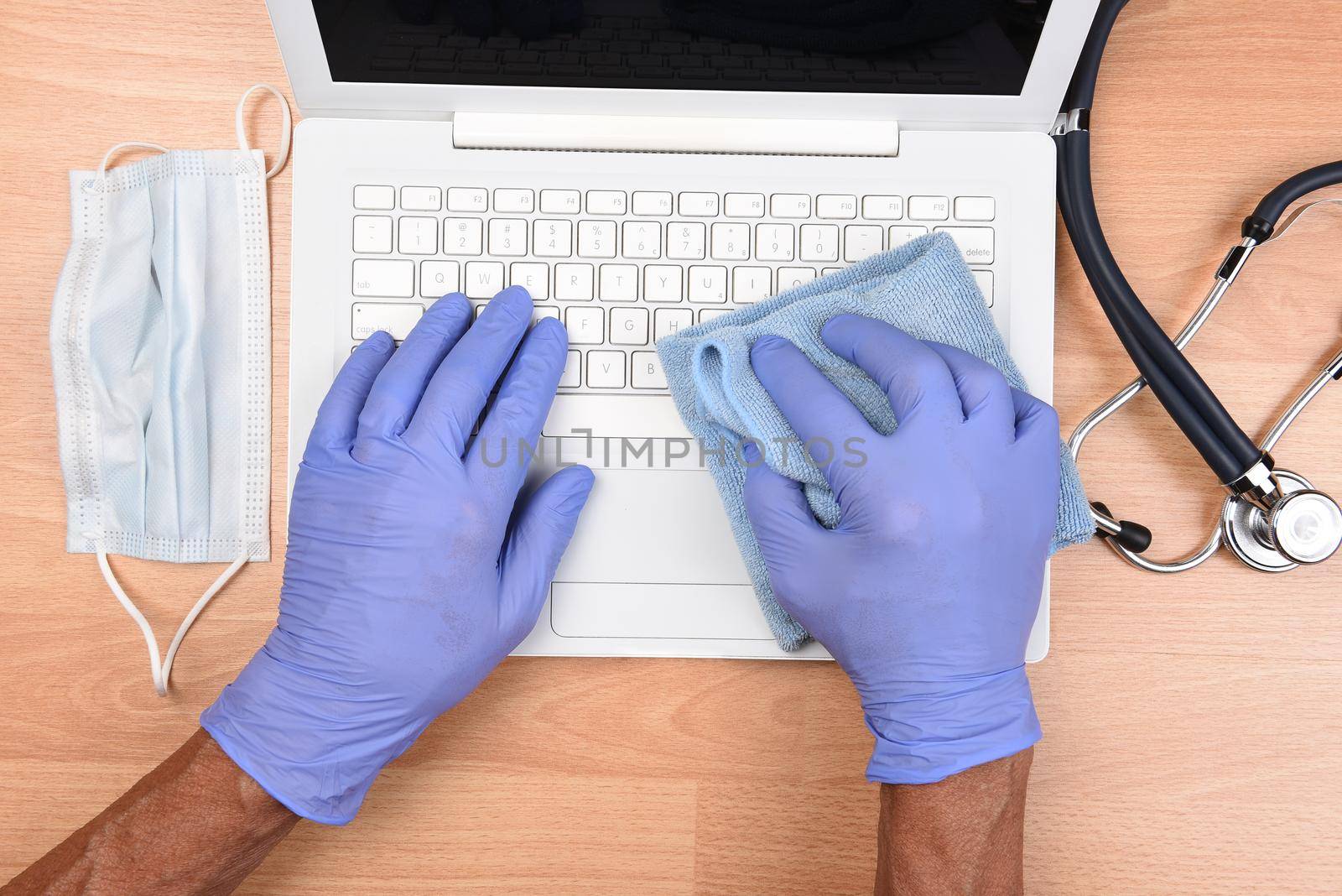 Medical professional with gloved hands disinfecting a laptop computer keyboard from virus, microbes and dirt. CovID-19 Prevention. by sCukrov