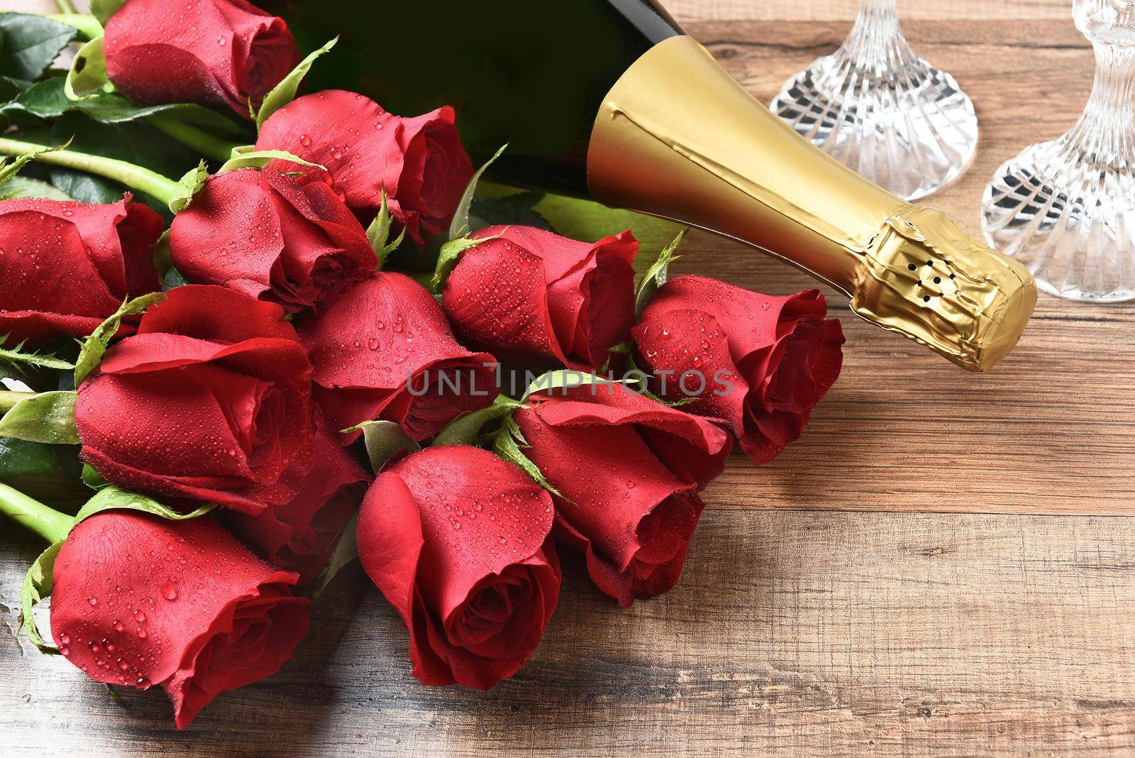 Closeup of a bottle of champagne and red roses on a wood table. Valentines Day / Love concept.