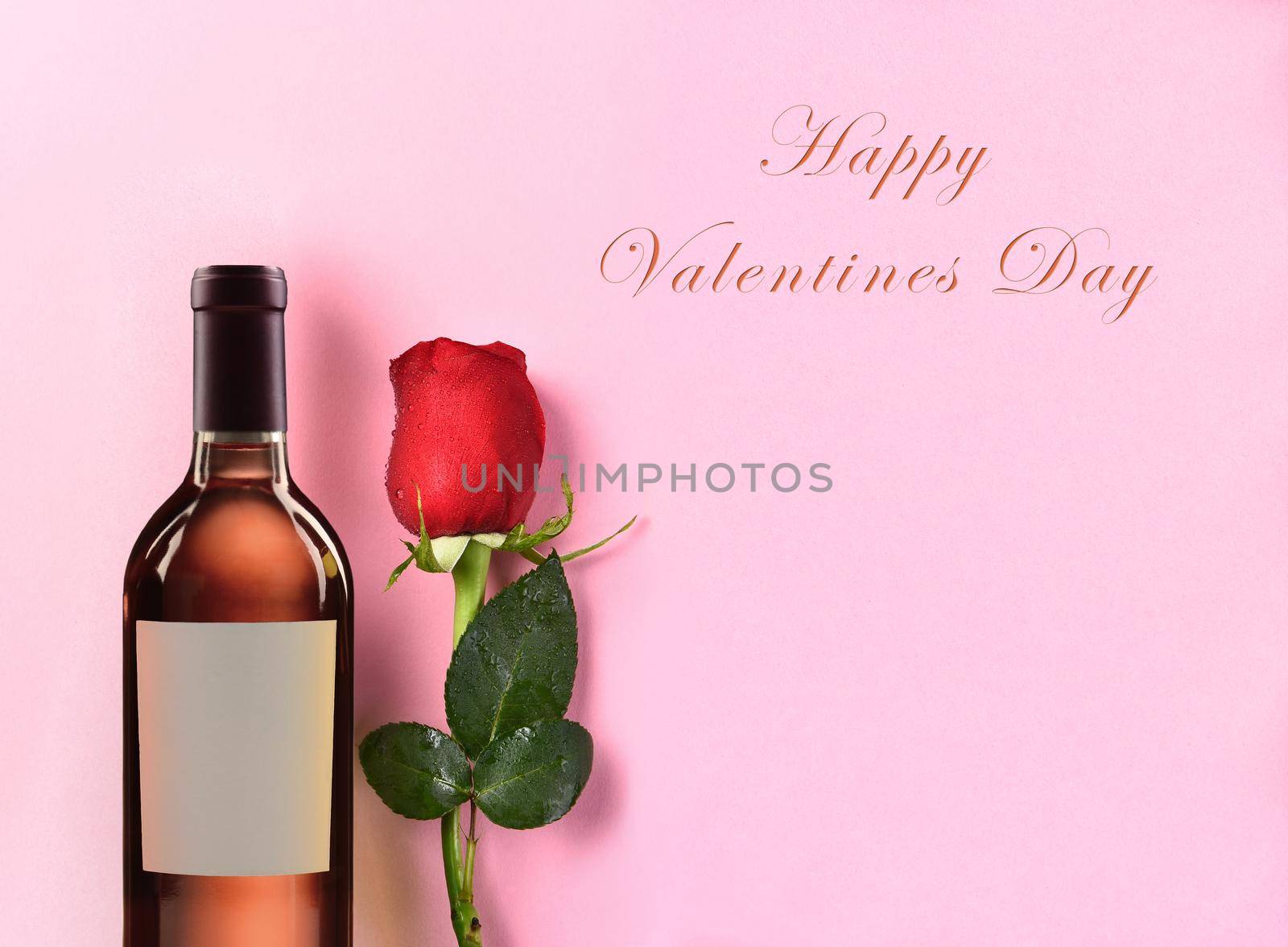 Happy Valentines Day closeup of a bottle of Blush Wine and a single red rose against a pink background.