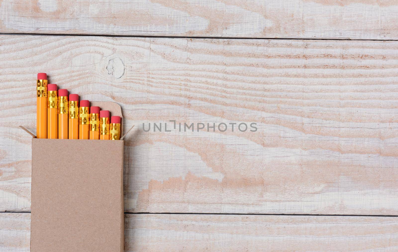 High angle shot of a cardboard box of new pencils on a whitewashed wood desk. The box is set ot the right leaving lots of copy space. Ideal for Back to School projects.