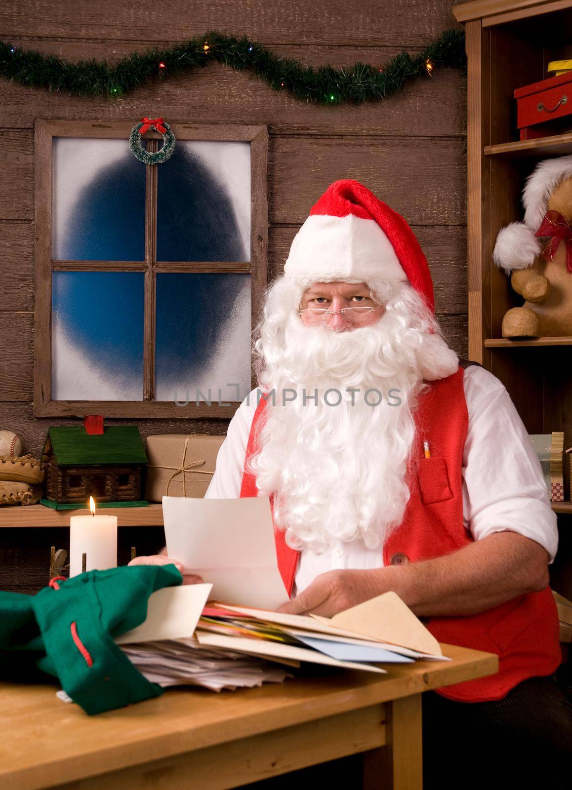 Santa Claus Sitting in His Workshop Painting reading letters. Vertical Composition.