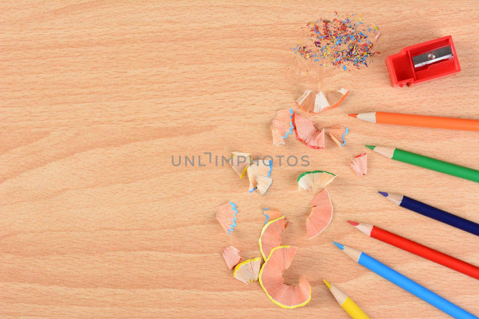 High angle view of six colored pencils on a school desk with a sharpener and shavings. Horizontal with copy space. Back to school concept.