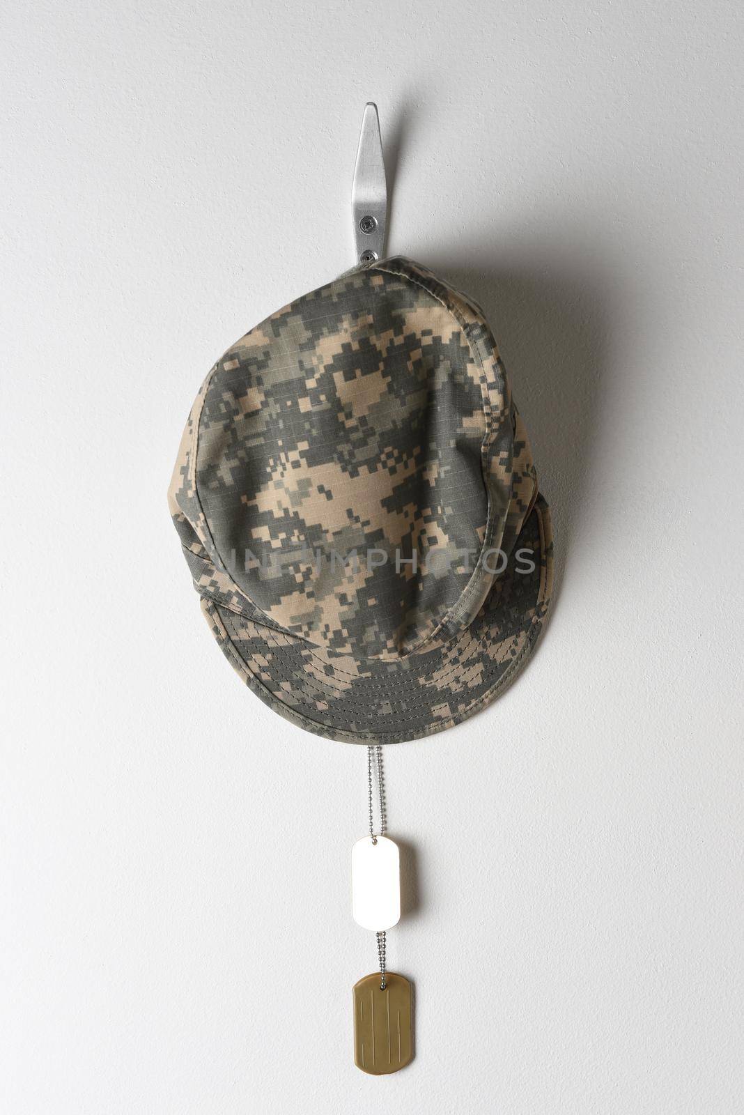 A set of military dog tags and field cap hanging from a hook on a blank wall.