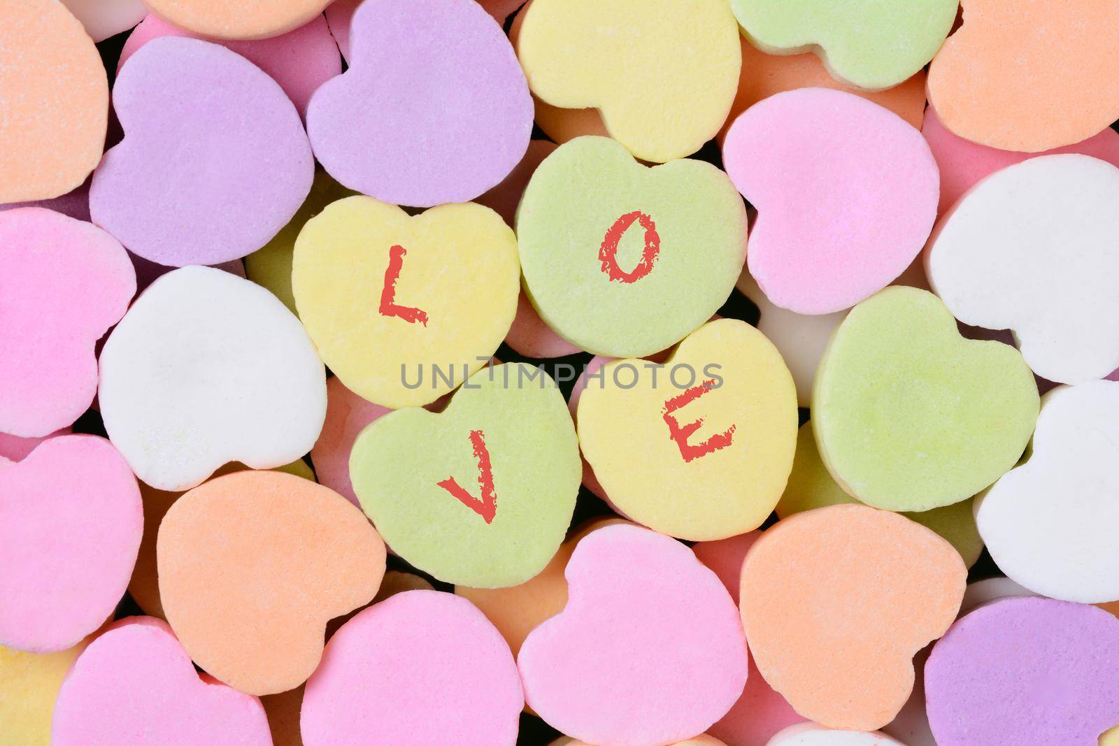 Macro shot of pastel candy hearts for Valentine's Day. Four of the candies have the word LOVE spelled out in individual letters. 