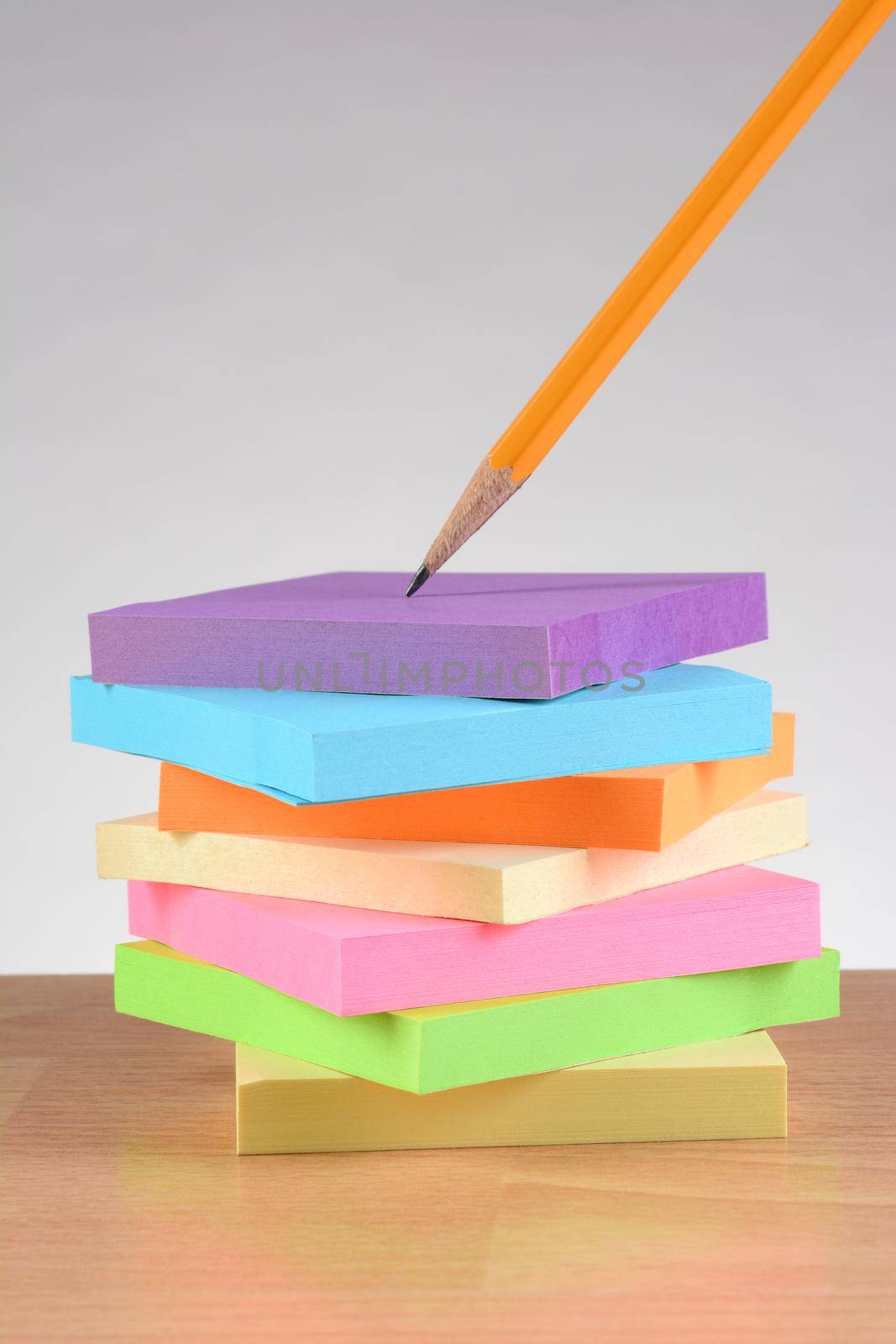 Colorful note pads and pencil on teachers desk. Vertical format against a light to dark gray background. 