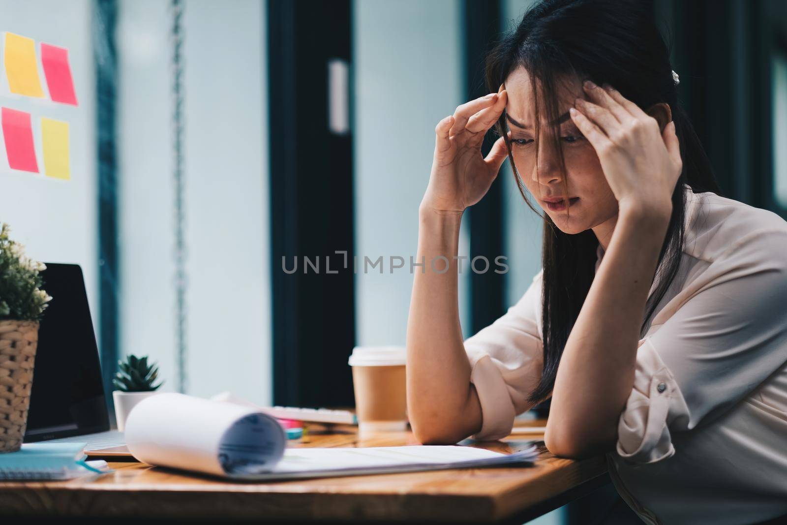 Tired young asian woman feel headache from working problem. Stressed female suffer from headache bad vision sight problem sit at workplace. by nateemee