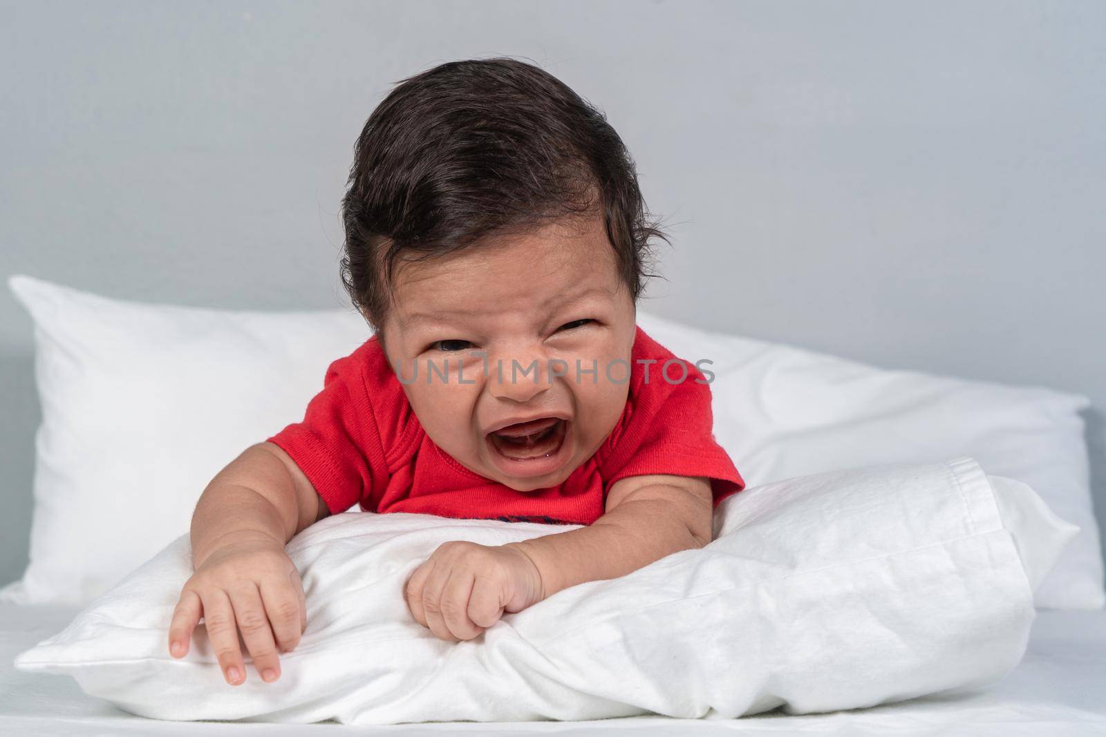 Infant with a crying expression, lying on his stomach with his head raised