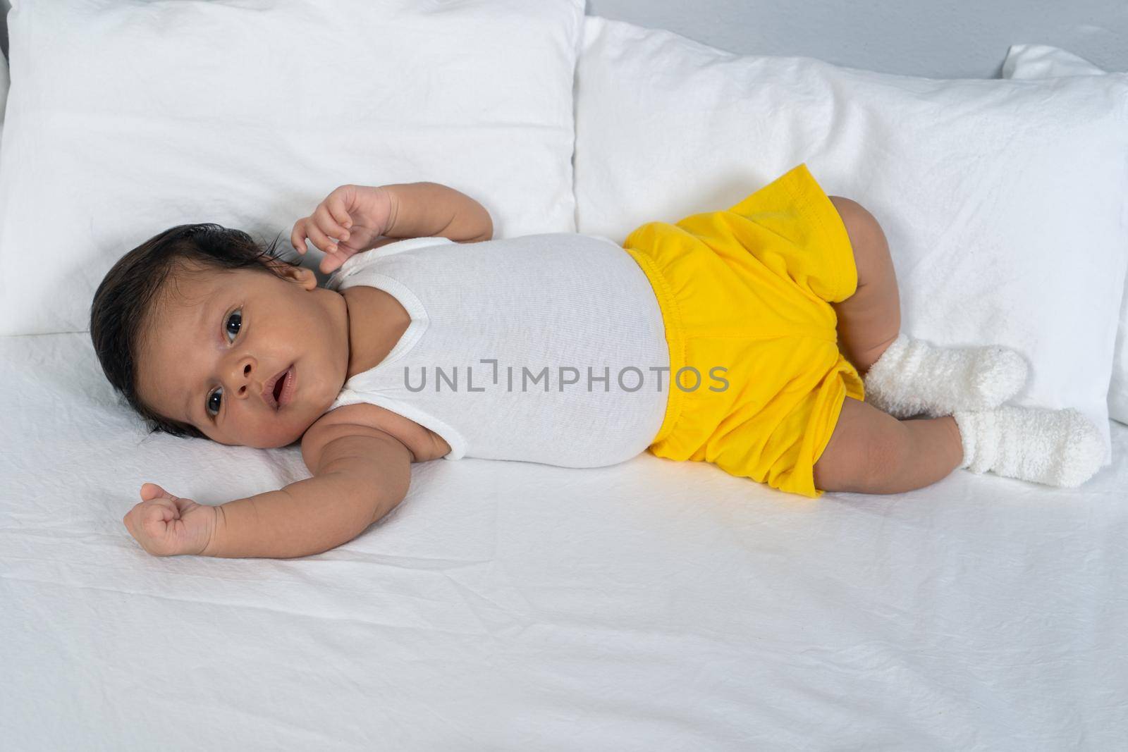 Infant lying on his back wearing a white t-shirt and yellow shorts