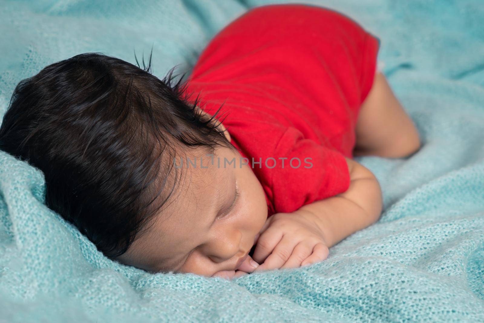 Baby sleeping on his stomach, dressed in red clothes