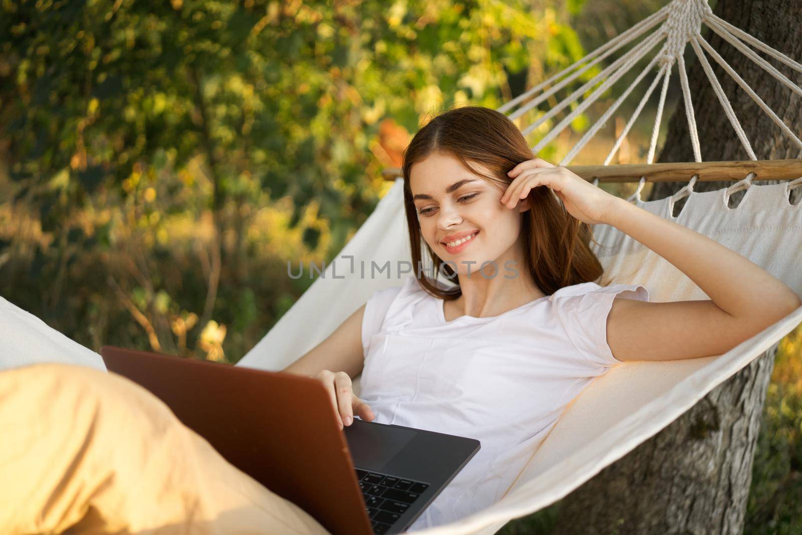 women outdoors lies in a hammock with a laptop freelance internet by Vichizh