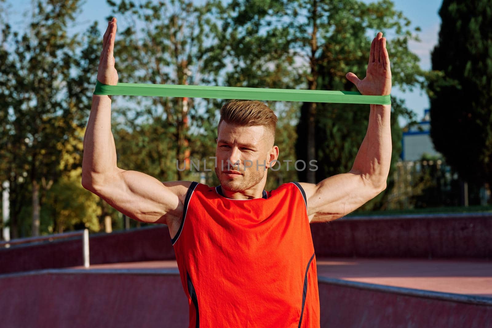 athletic man on the sports ground rubber band exercise by Vichizh