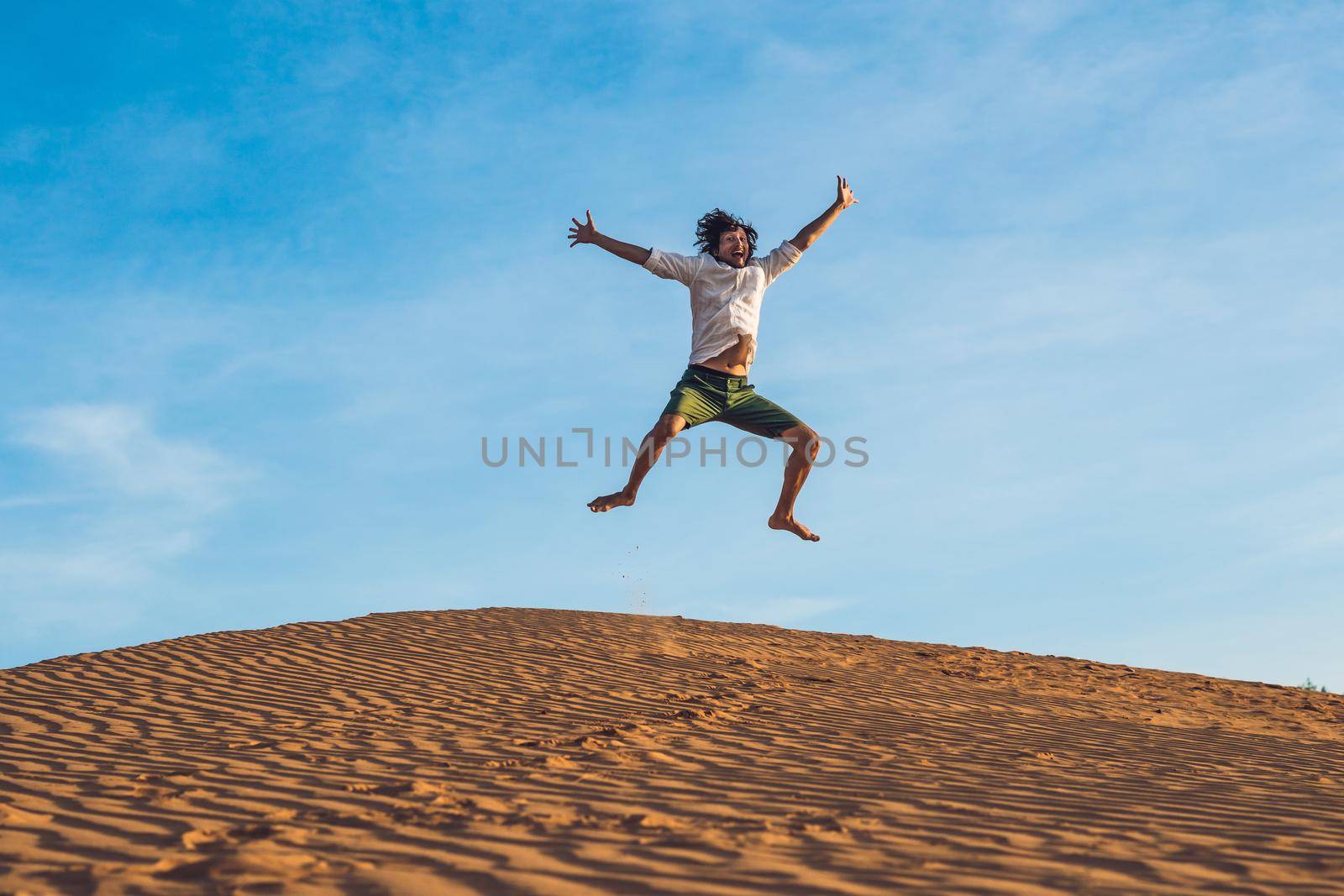 Beautiful young man jumping barefoot on sand in desert enjoying nature and the sun. Fun, joy and freedom by galitskaya