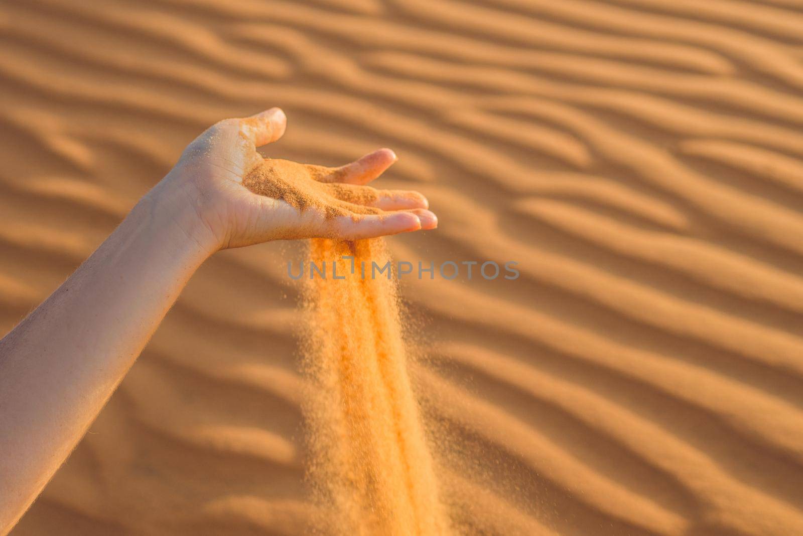Sand slipping through the fingers of a woman's hand in the desert.