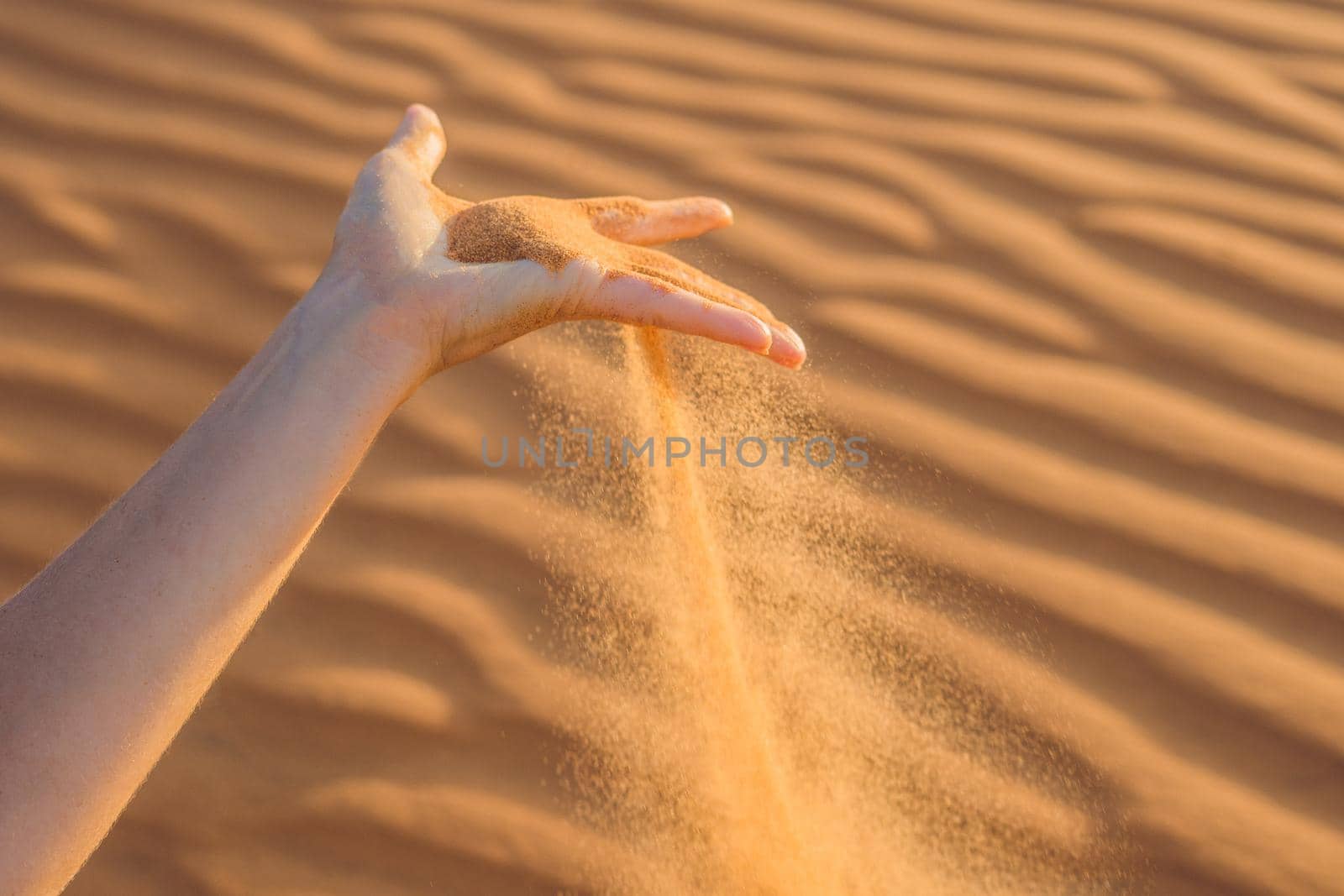 Sand slipping through the fingers of a woman's hand in the desert.
