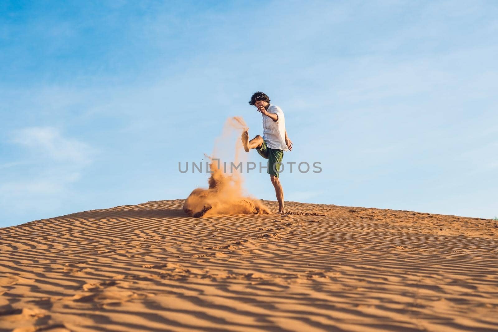 A man is kicking sand in a red desert. Splash of anger concept.