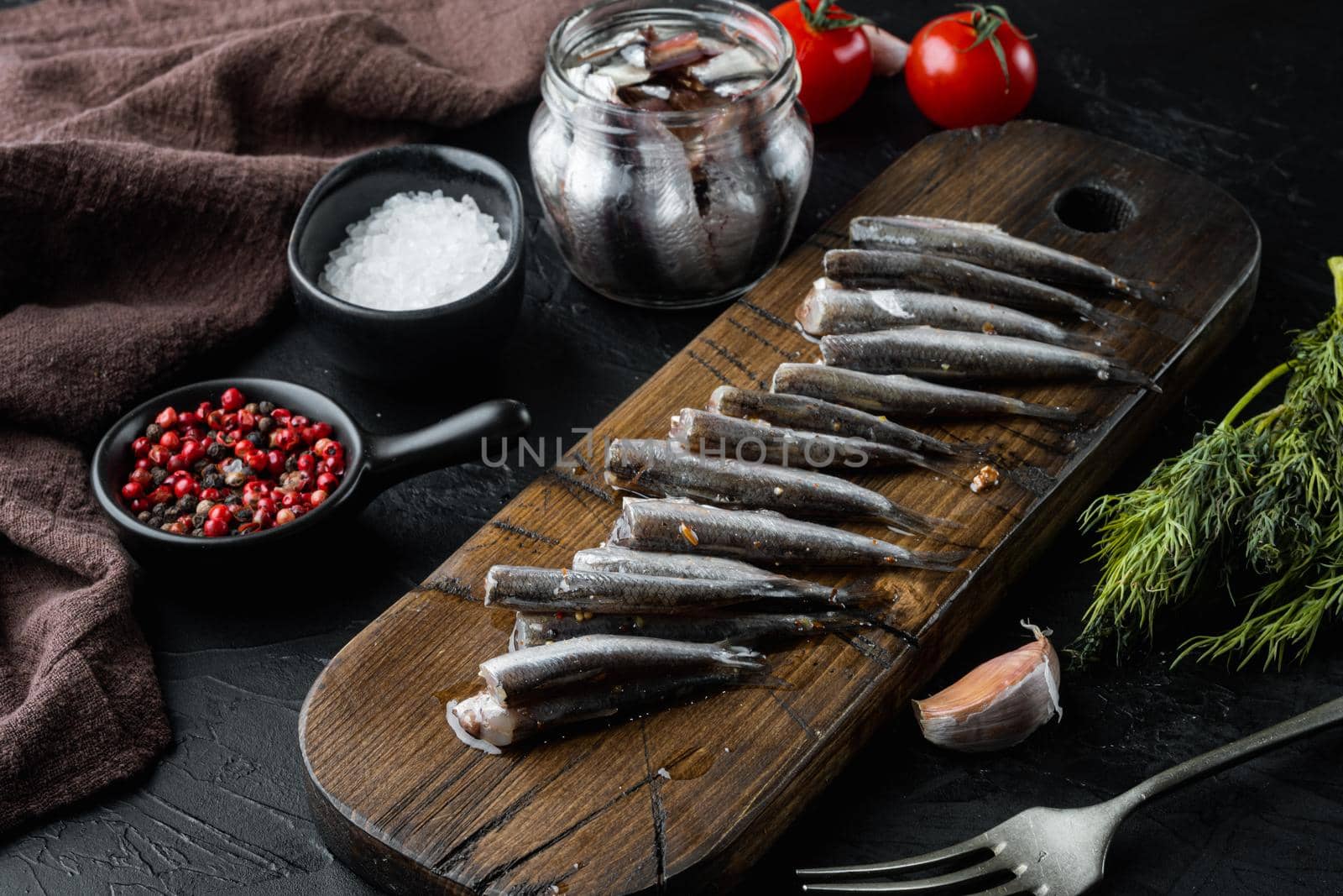 Salted anchovy fillets set, on wooden cutting board, on black background with herbs and ingredients