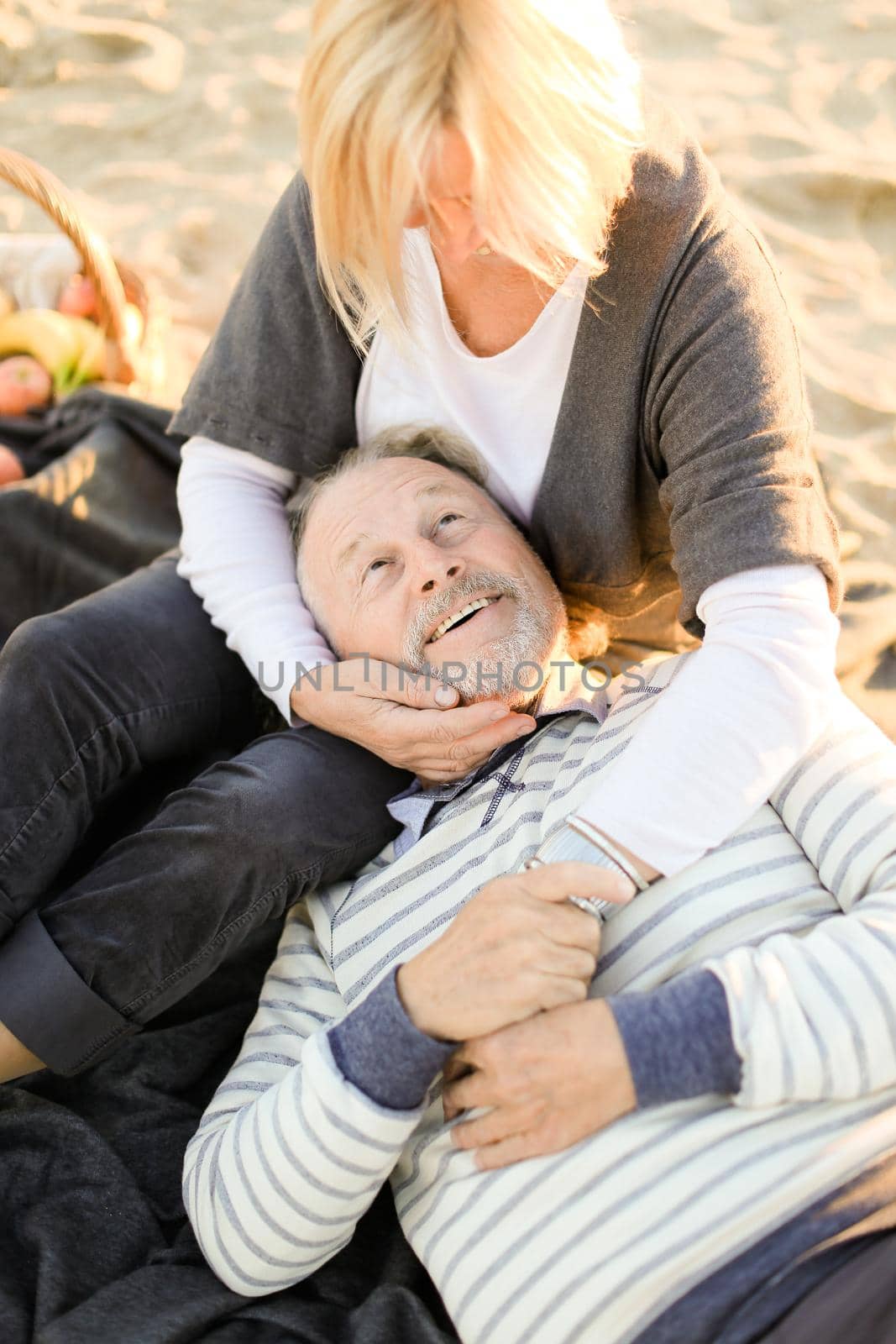Senior husband lying on wife knees, sand beach in background. by sisterspro