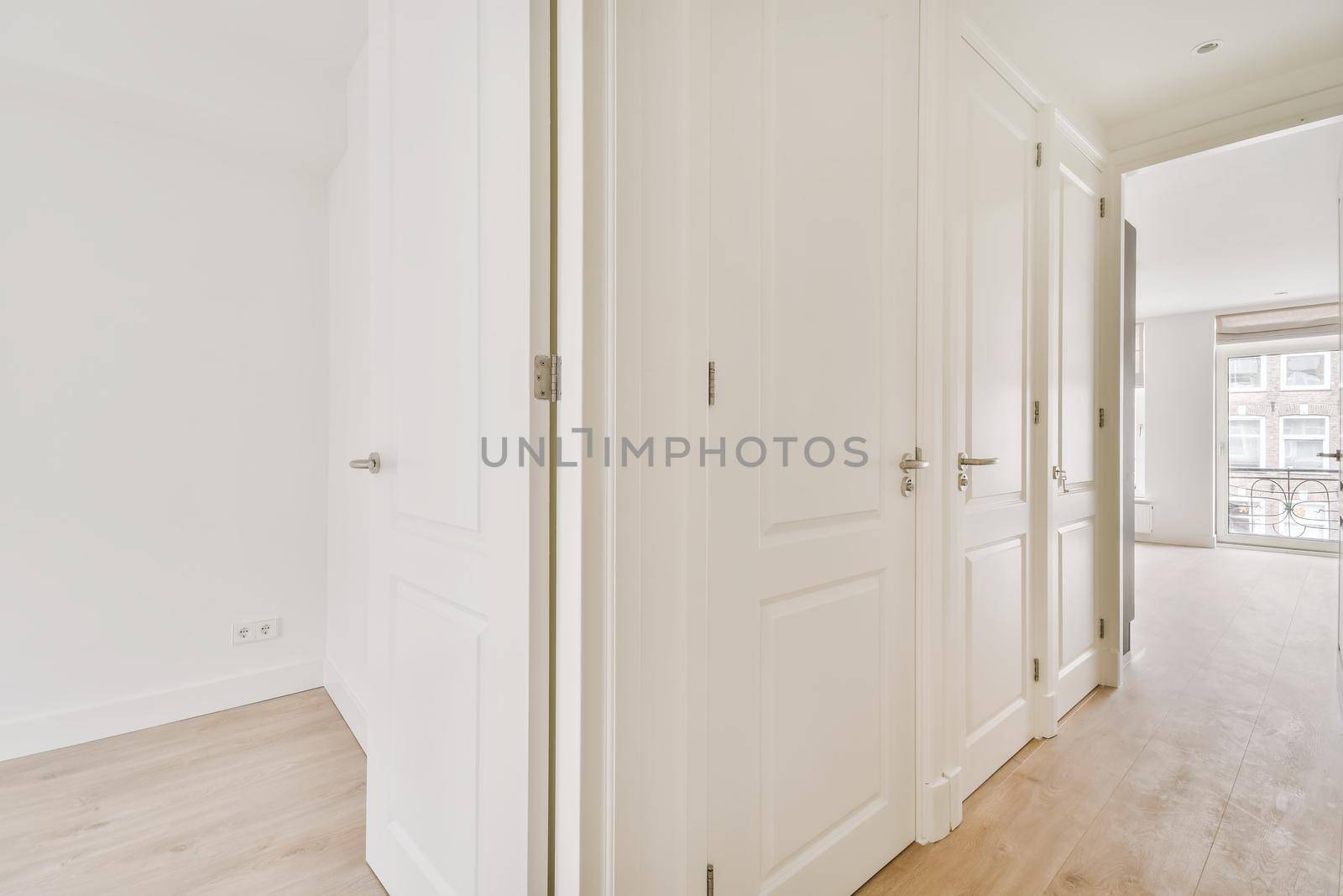 A perspective view of an empty narrow hallway with white walls and parquet floors in a minimalist apartment.