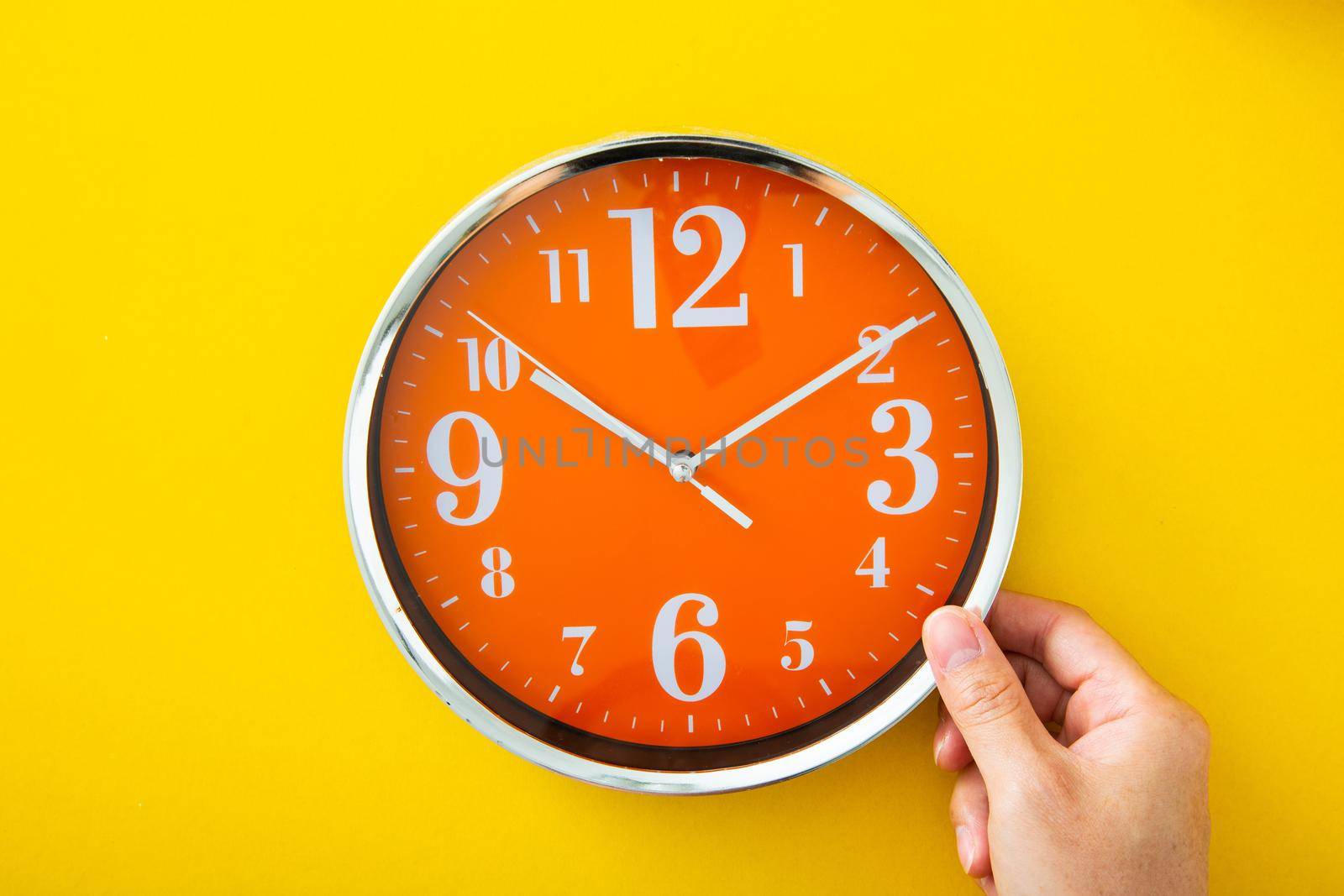 Hand holding alarm clock on isolated yellow background.