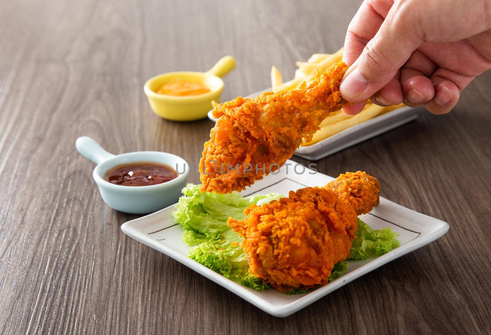 hand holding crispy and golden fried chickens with sauce on wooden table