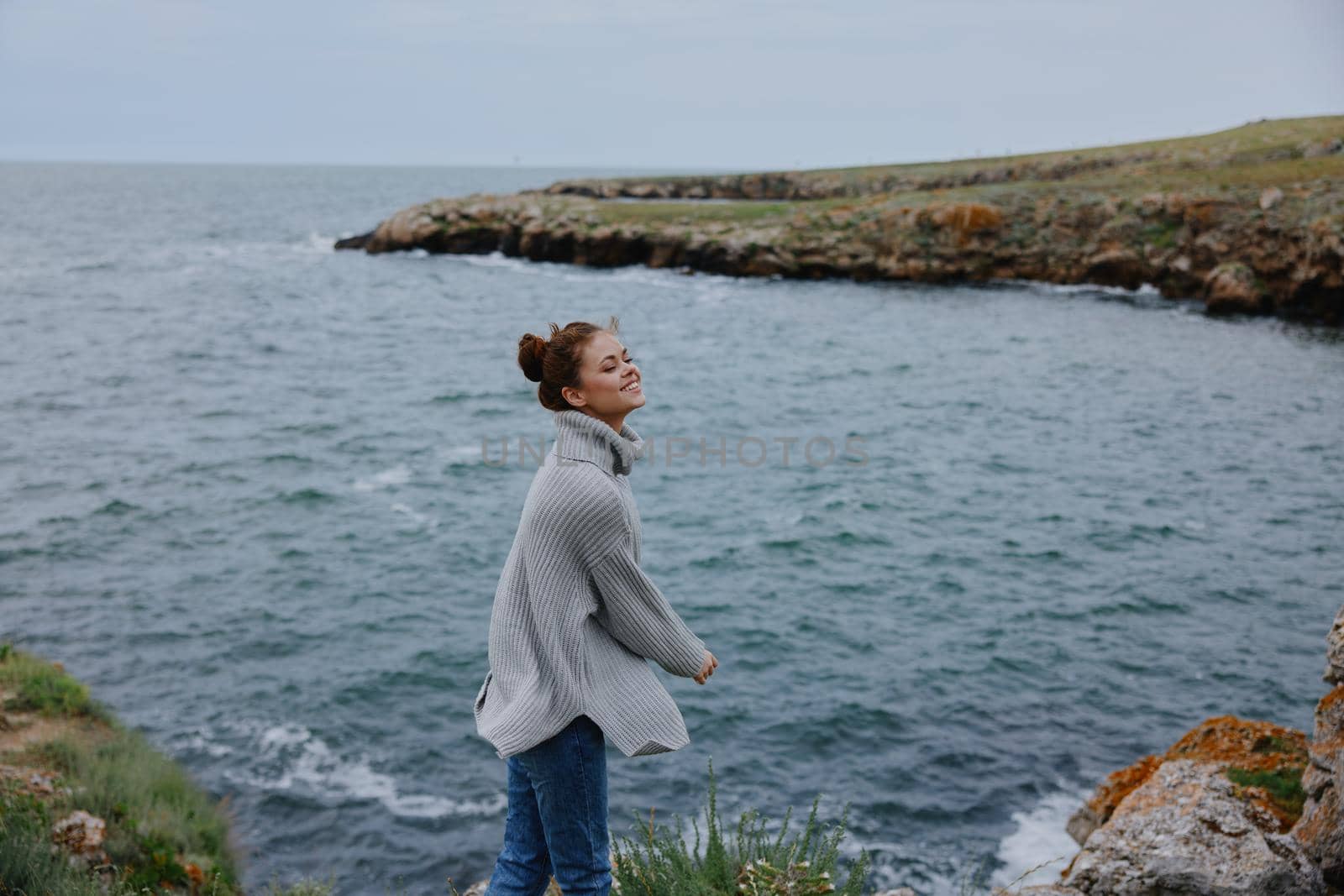 woman in a gray sweater stands on a rocky shore nature Lifestyle. High quality photo