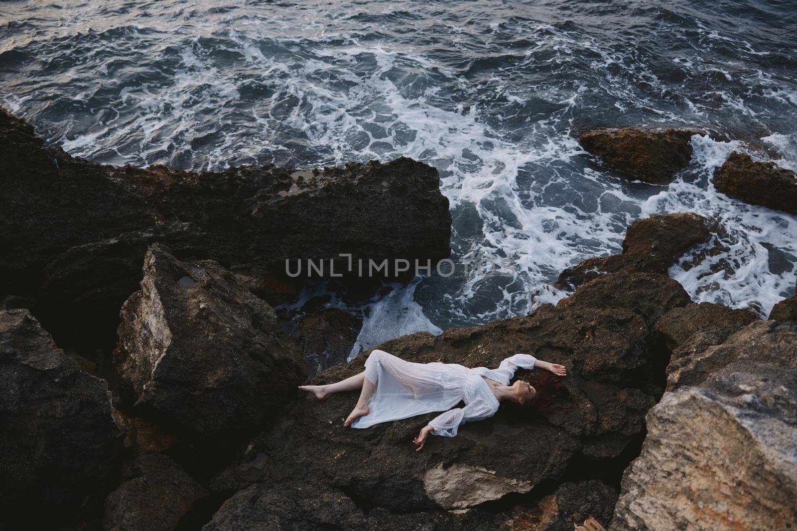 Beautiful bride in long white dress wet hair lying on a rocky cliff unaltered by SHOTPRIME