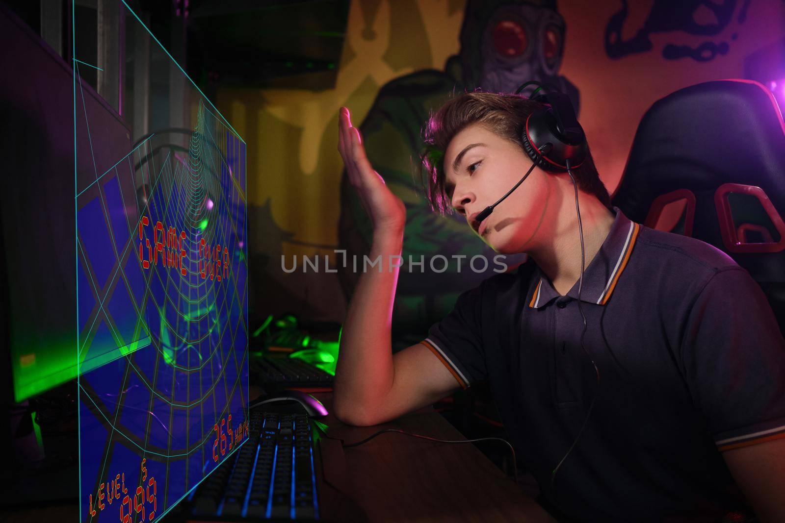 Photo of professional young caucasian gamer playing online on his PC in gaming club or cyber arena. He looks displeased and upset. Game plan went wrong. laser screen, projector, augmented reality, AR, VR