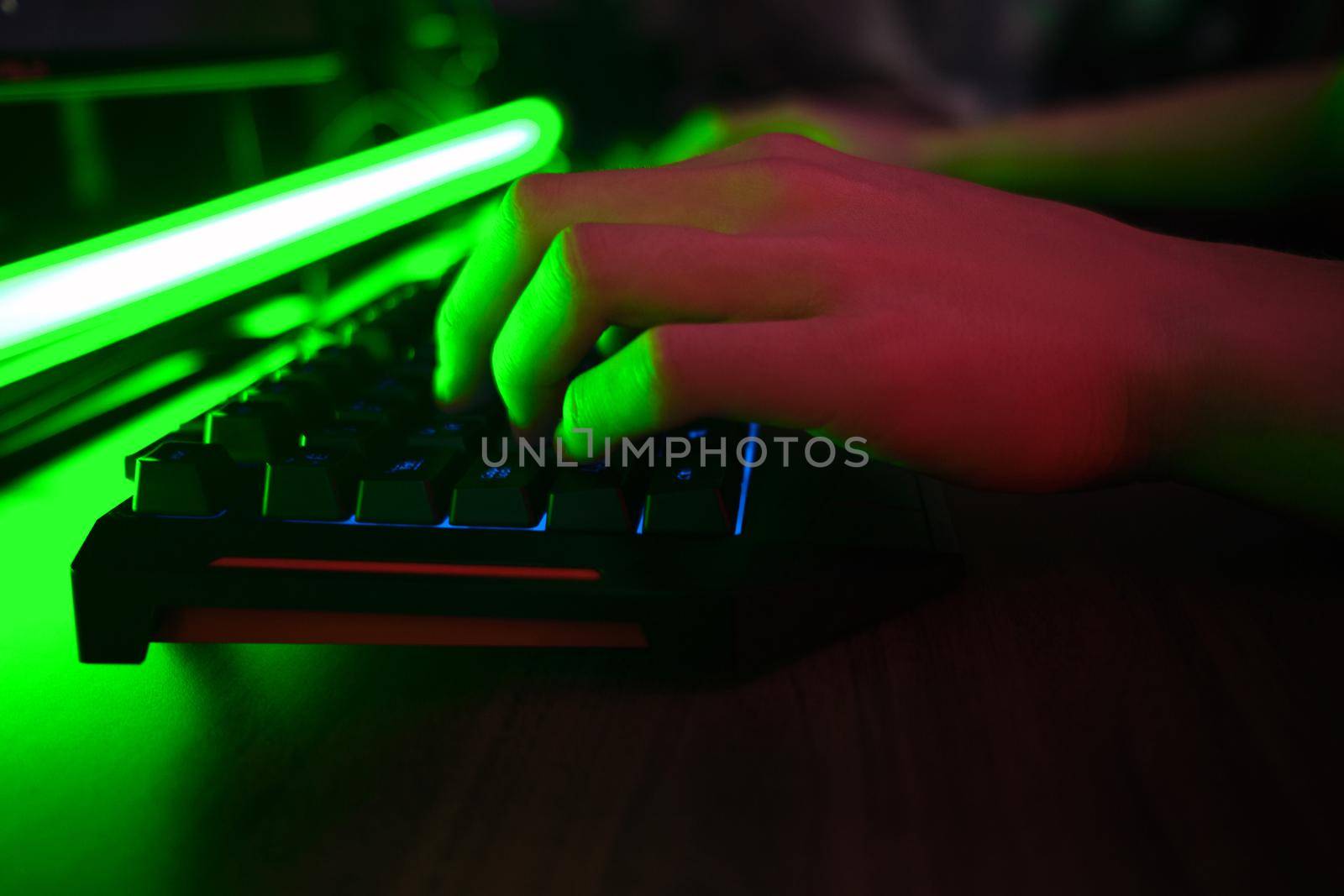 Close up view of professional players hands on gaming keyboard in gaming club or cyber arena. Green neon light