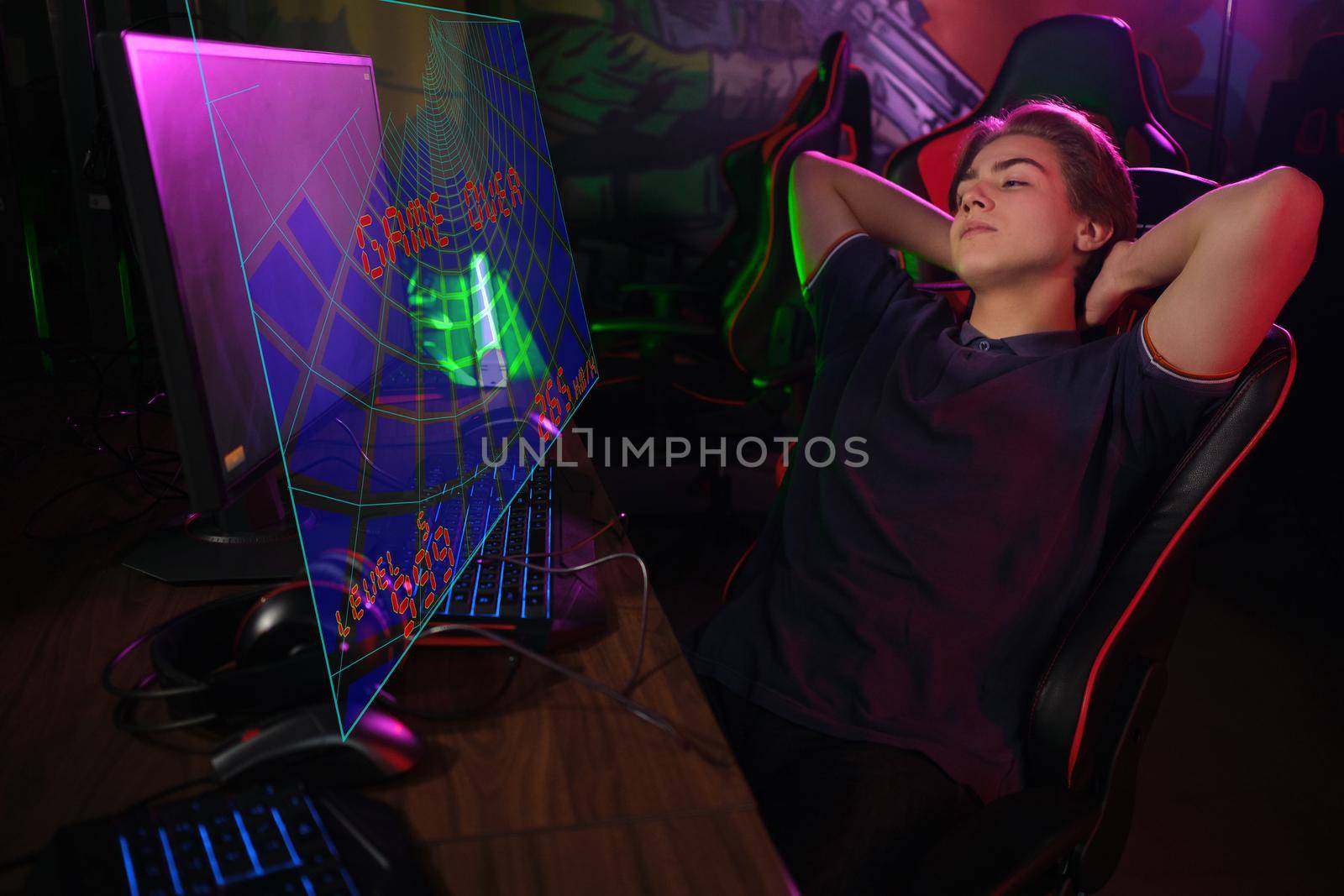Professional photo of young male caucasian cyber sportsman in gaming club waiting for another match, relaxing on his gaming chair.. laser screen, projector, augmented reality, AR, VR