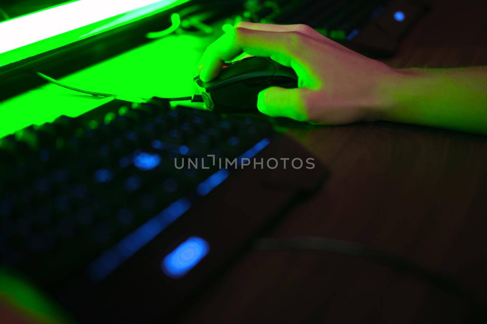 Close up view of professional players hands on gaming mouse in gaming club or cyber arena. Green neon light