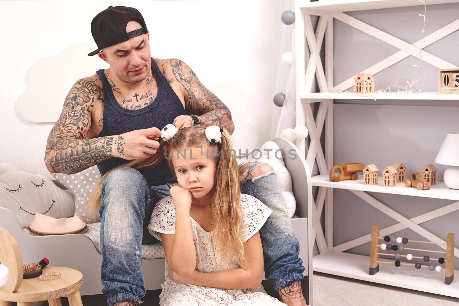 Funny time Tattoed father in a cap and his child are playing at home. Dad is doing his daughter's hair in her bedroom. Family holiday and togetherness by nazarovsergey