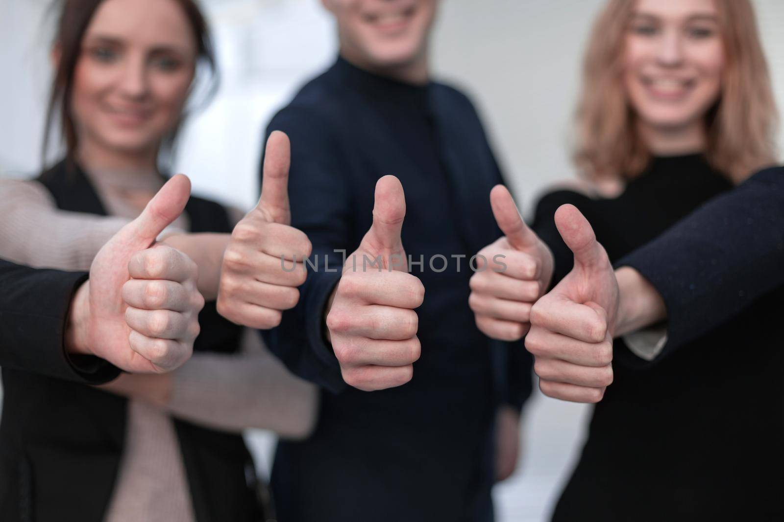 Close-up of group of business people raising their arms up and showing thumbs up