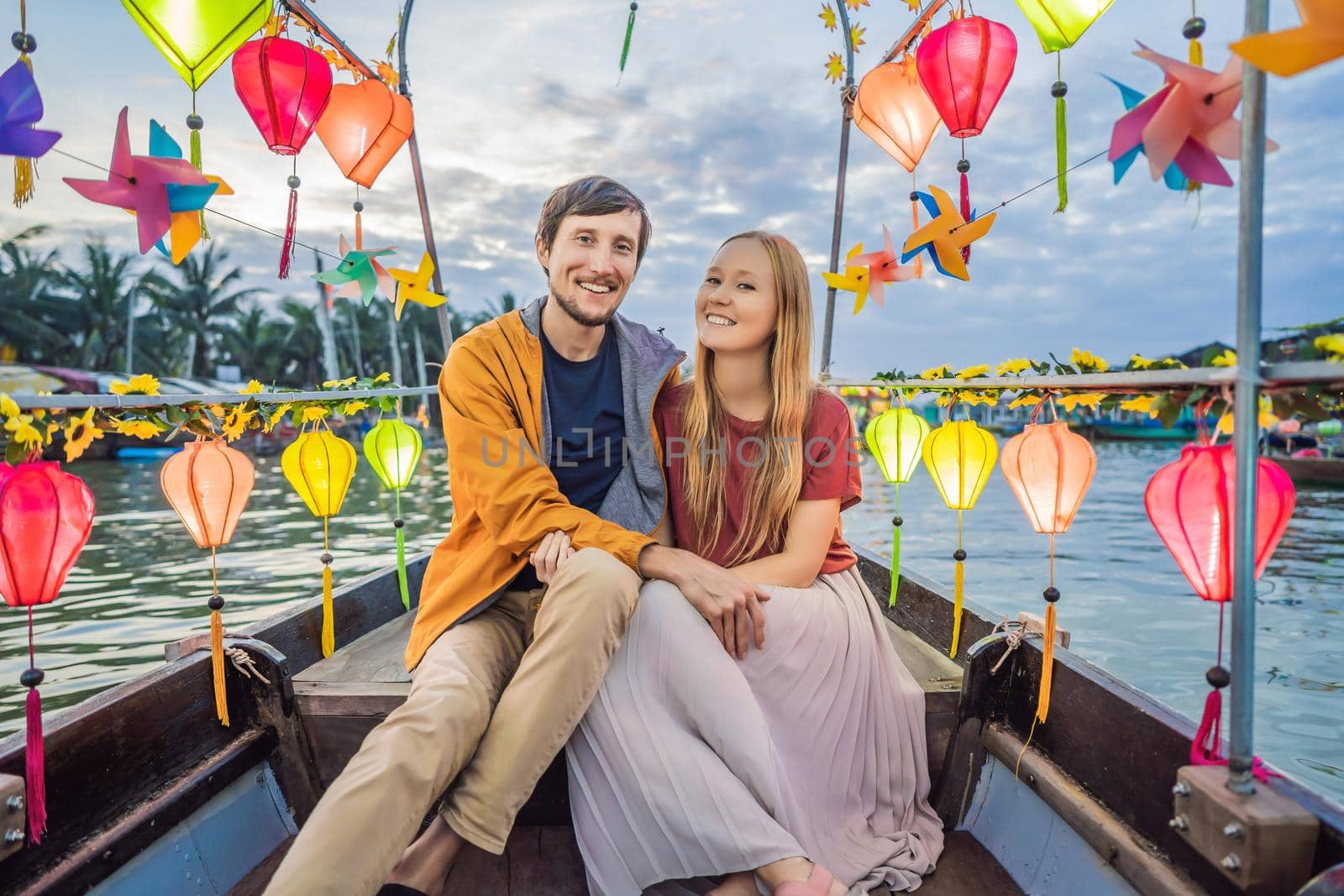 Happy couple of travelers ride a national boat on background of Hoi An ancient town, Vietnam. Vietnam opens to tourists again after quarantine Coronovirus COVID 19.