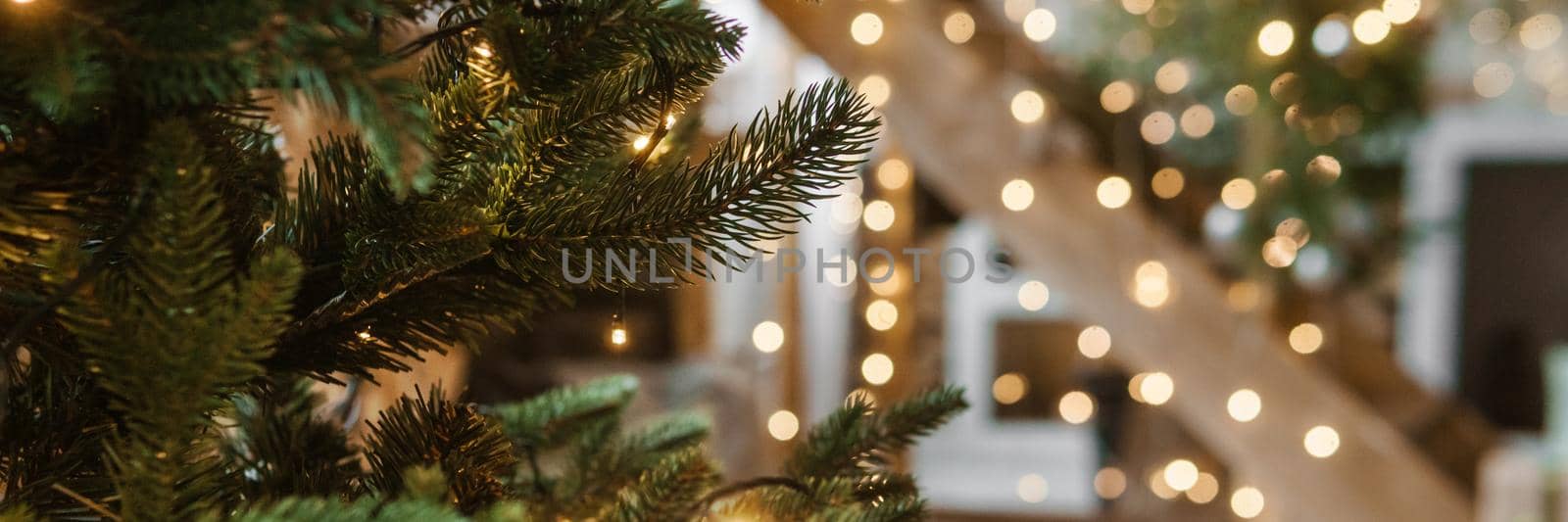 Home New Year's interior. A live Christmas tree and a wooden staircase in the kitchen. Cozy atmosphere of a home holiday, loft design of the room, daylight, green tree decorated with lights. Modern Scandinavian style in the interior. The eve of December 25th.