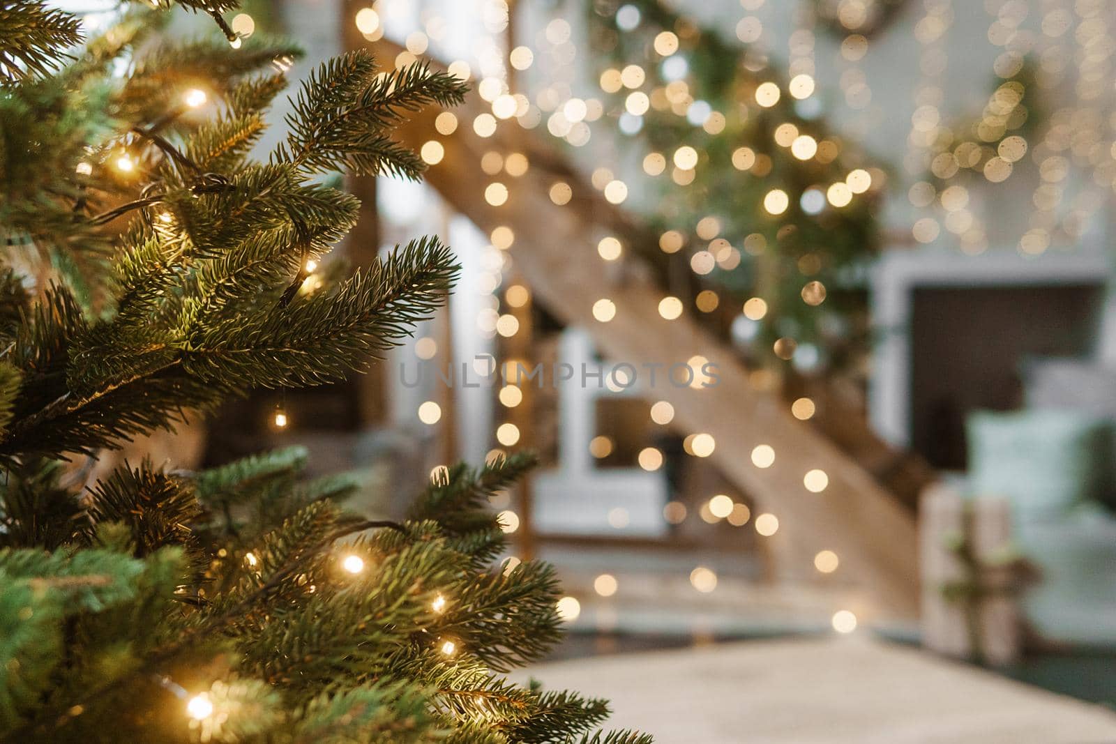 Home New Year's interior. A live Christmas tree and a wooden staircase in the kitchen. Cozy atmosphere of a home holiday, loft design of the room, daylight, green tree decorated with lights. Modern Scandinavian style in the interior. The eve of December 25th.
