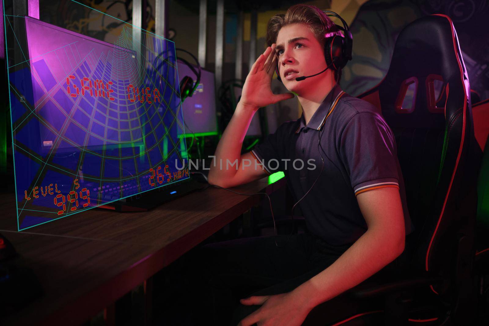 Photo of professional young caucasian gamer playing online on his PC in gaming club or cyber arena. He looks displeased and upset. Game plan went wrong. laser screen, projector, augmented reality, AR, VR
