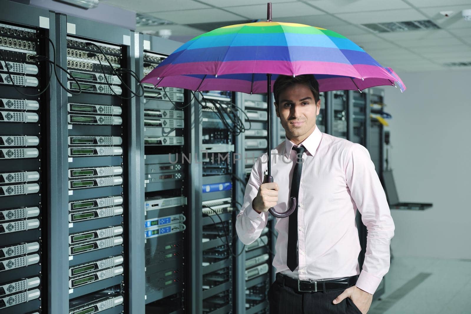 young handsome business man  engineer in 
businessman hold  rainbow colored umbrella in server datacenter room  and representing security and antivirus sofware protection concept