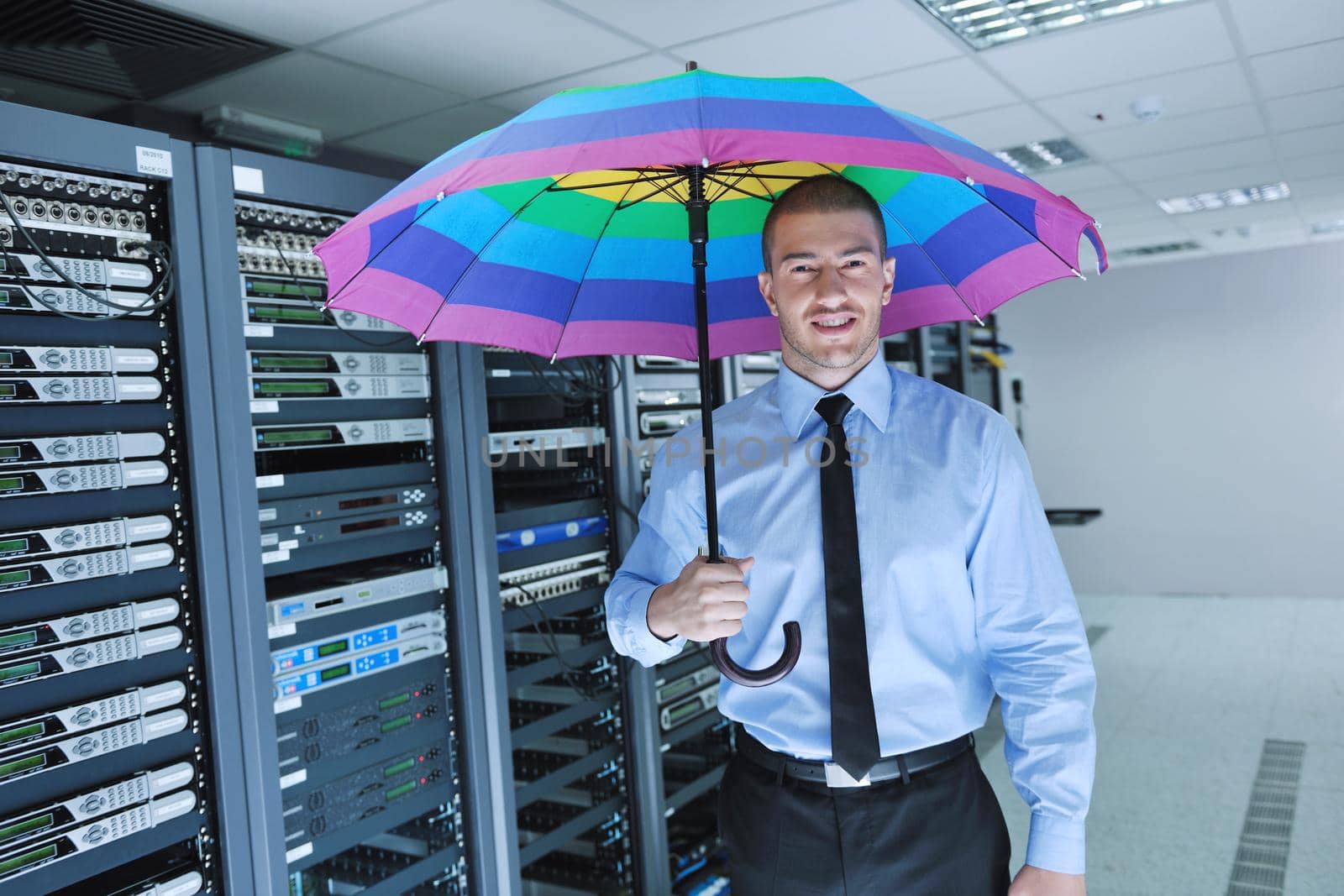 young handsome business man  engineer in 
businessman hold  rainbow colored umbrella in server datacenter room  and representing security and antivirus sofware protection concept