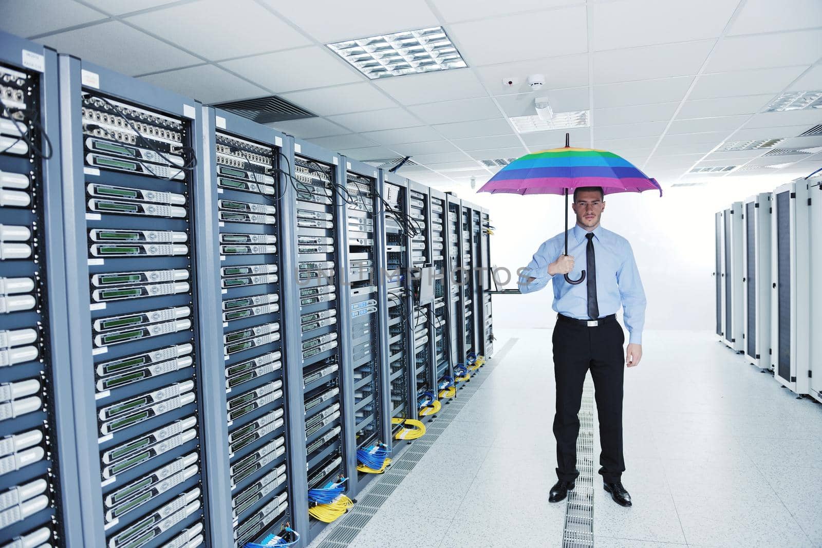 young handsome business man  engineer in 
businessman hold  rainbow colored umbrella in server datacenter room  and representing security and antivirus sofware protection concept