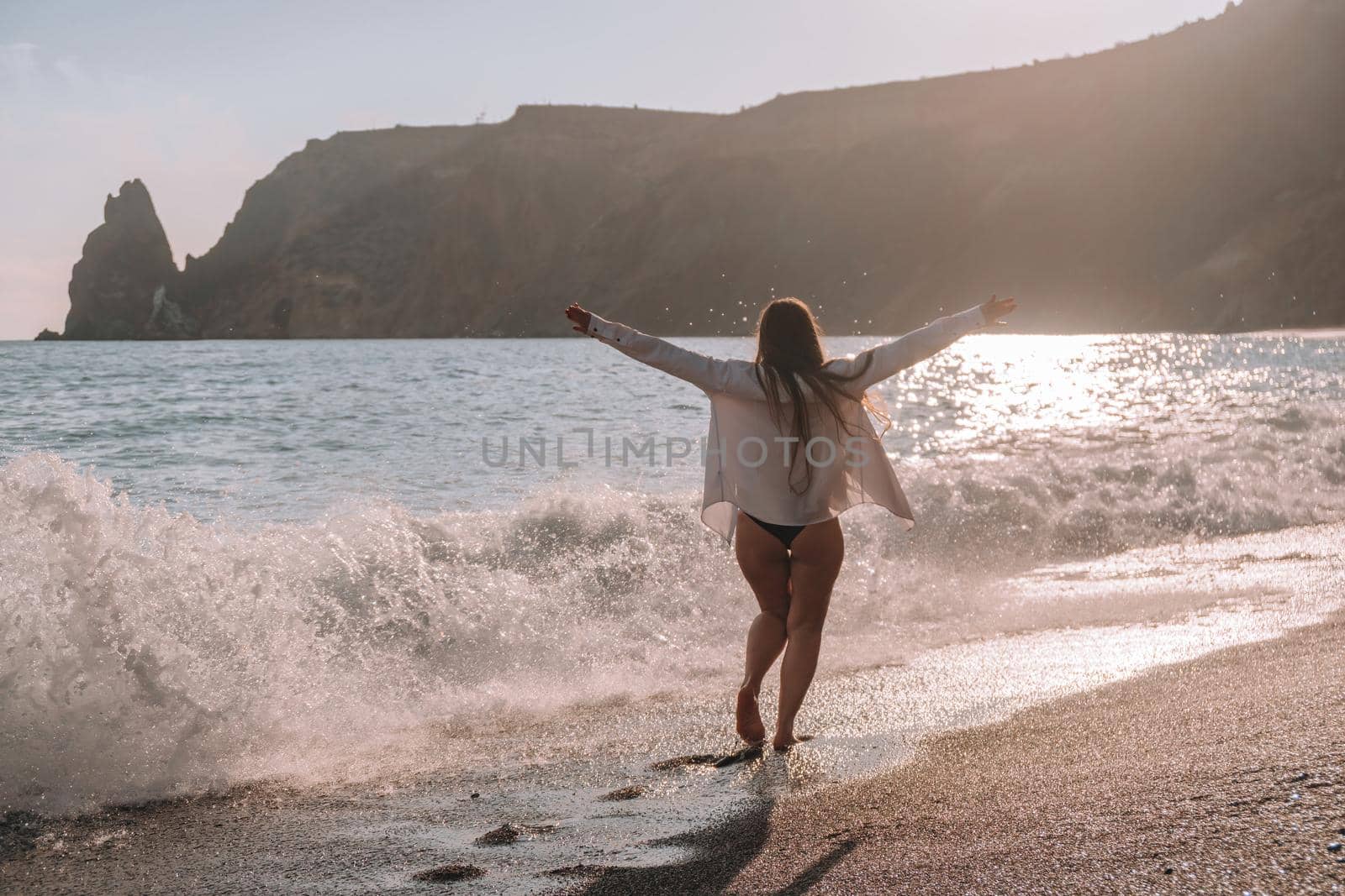 Selective focus. Happy carefree sensual woman with long hair in black swimwear posing at sunset beach. Silhouette of young beautiful playful positive woman outdoor. Summer vacation and trip concept.