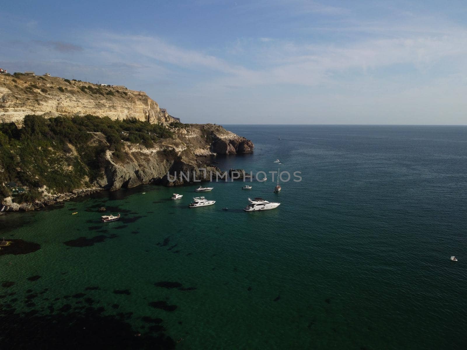 Sea landscape with rocky coastline on sunset time with cloudy sky. Yachts in the Sea on a background of rocky shores. The concept of perfect place for summer travel and rest.