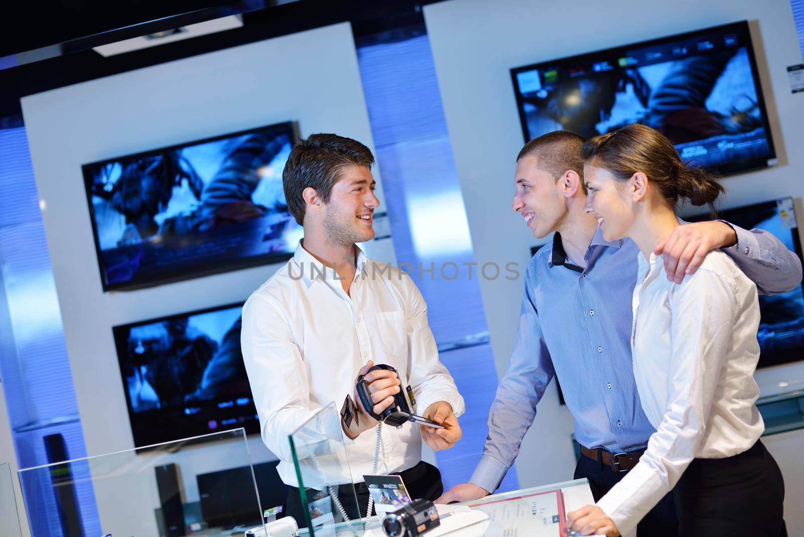 Young couple in consumer electronics store looking at latest laptop, television and photo camera to buy