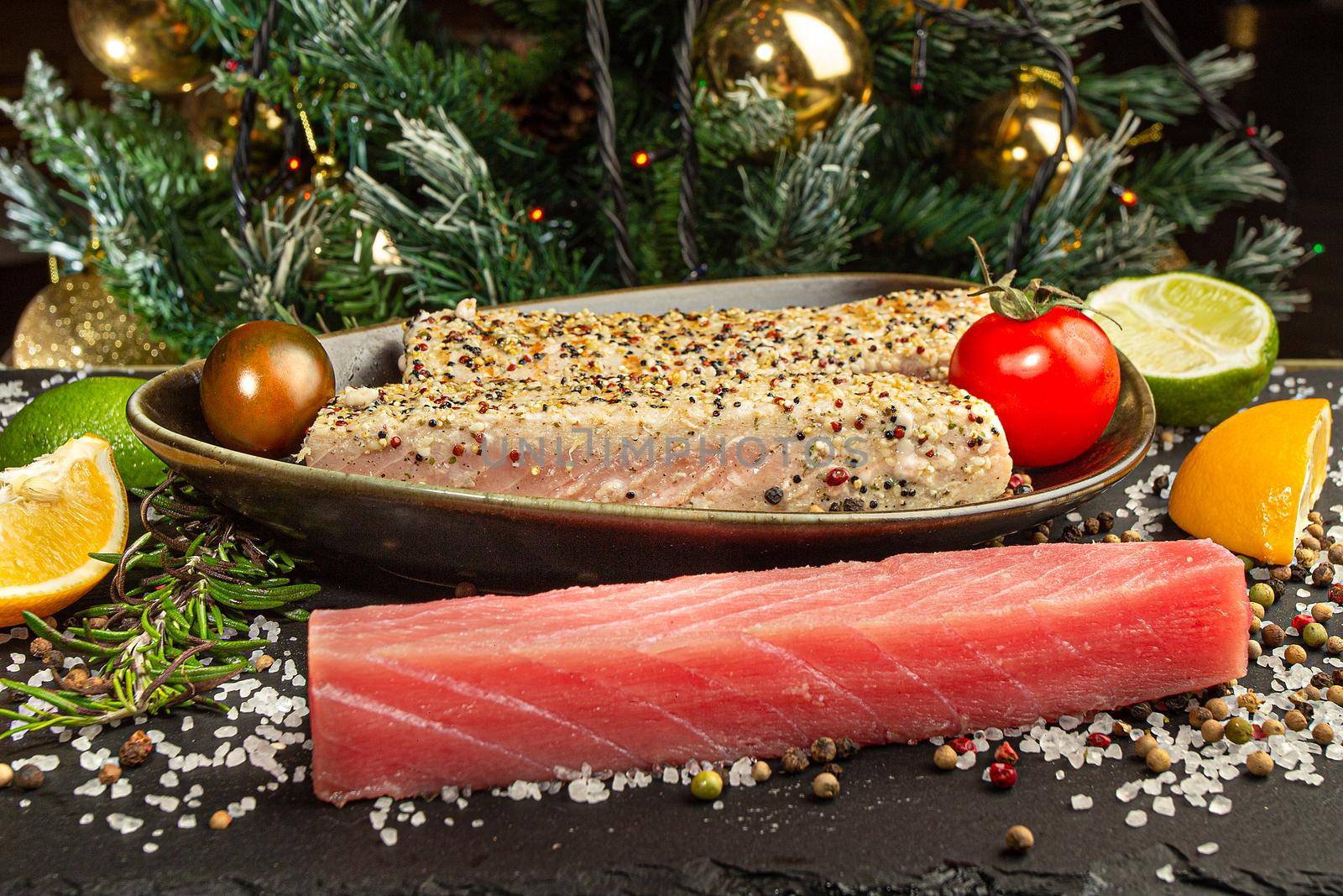 Stone slate tray with tuna steak fried in sesame seeds, tomatoes and citrus fruits, front view. Christmas and New Year background.